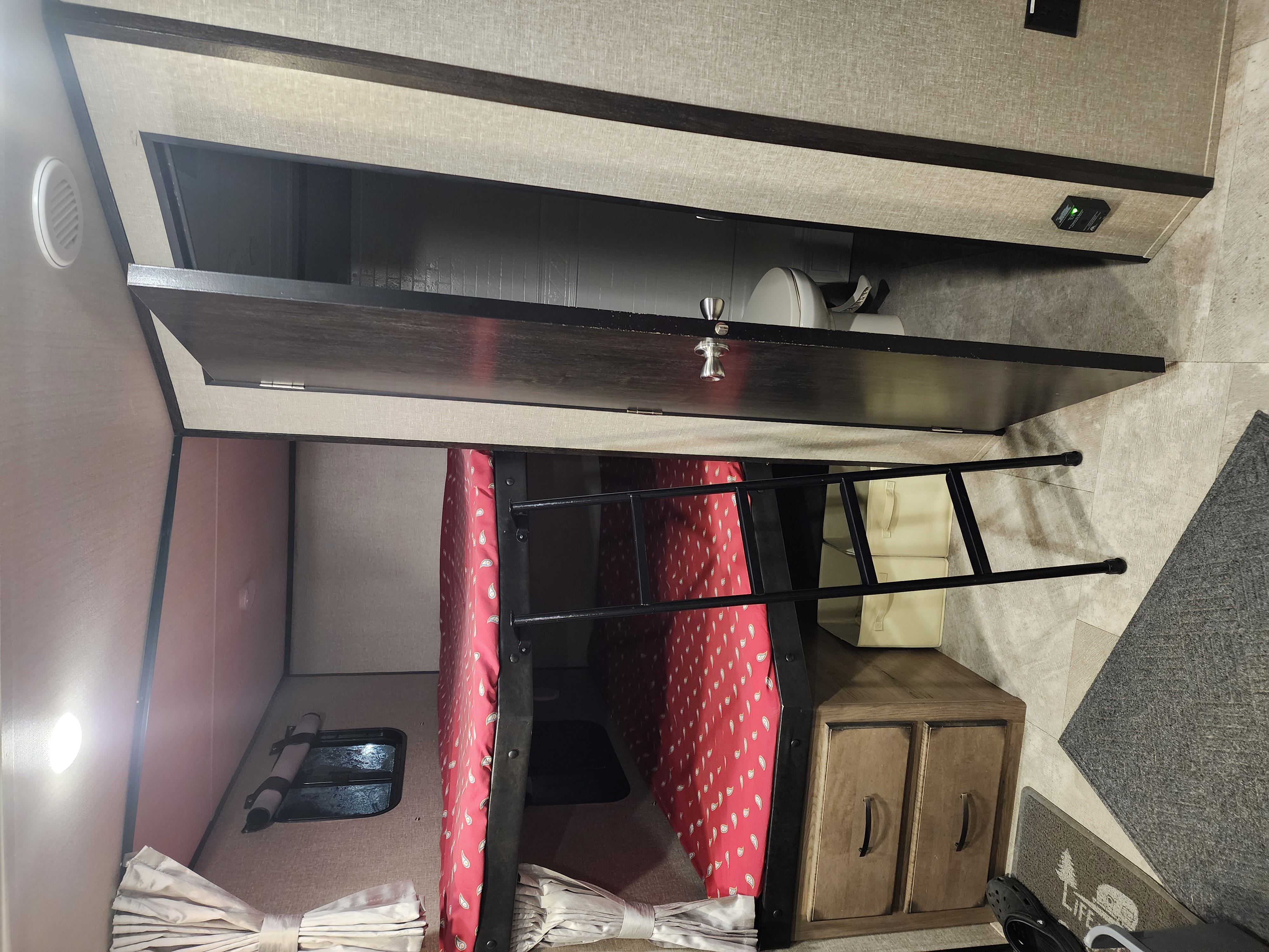 Inside an RV rental: bunk beds with red covers, a ladder, cabinet, and an open bathroom door showing the toilet.. Grand Design Transcend 2019