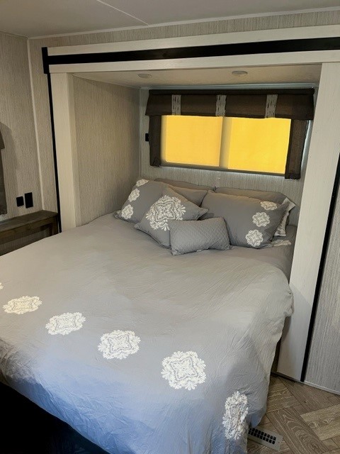 Inviting RV rental bedroom showcasing a comfortable bed with grey bedding, embroidered details, and a bright window.. Palomino Puma 26FKDS 2022