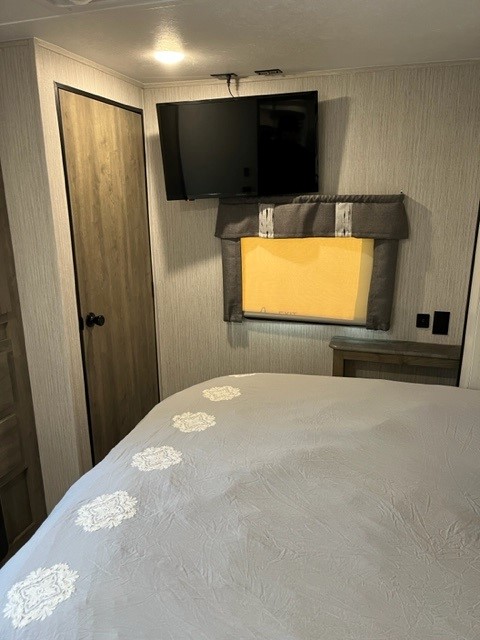 Bedroom in an RV rental featuring a wall-mounted TV, cozy bed, and closet door. Ideal for comfortable stays.. Palomino Puma 26FKDS 2022