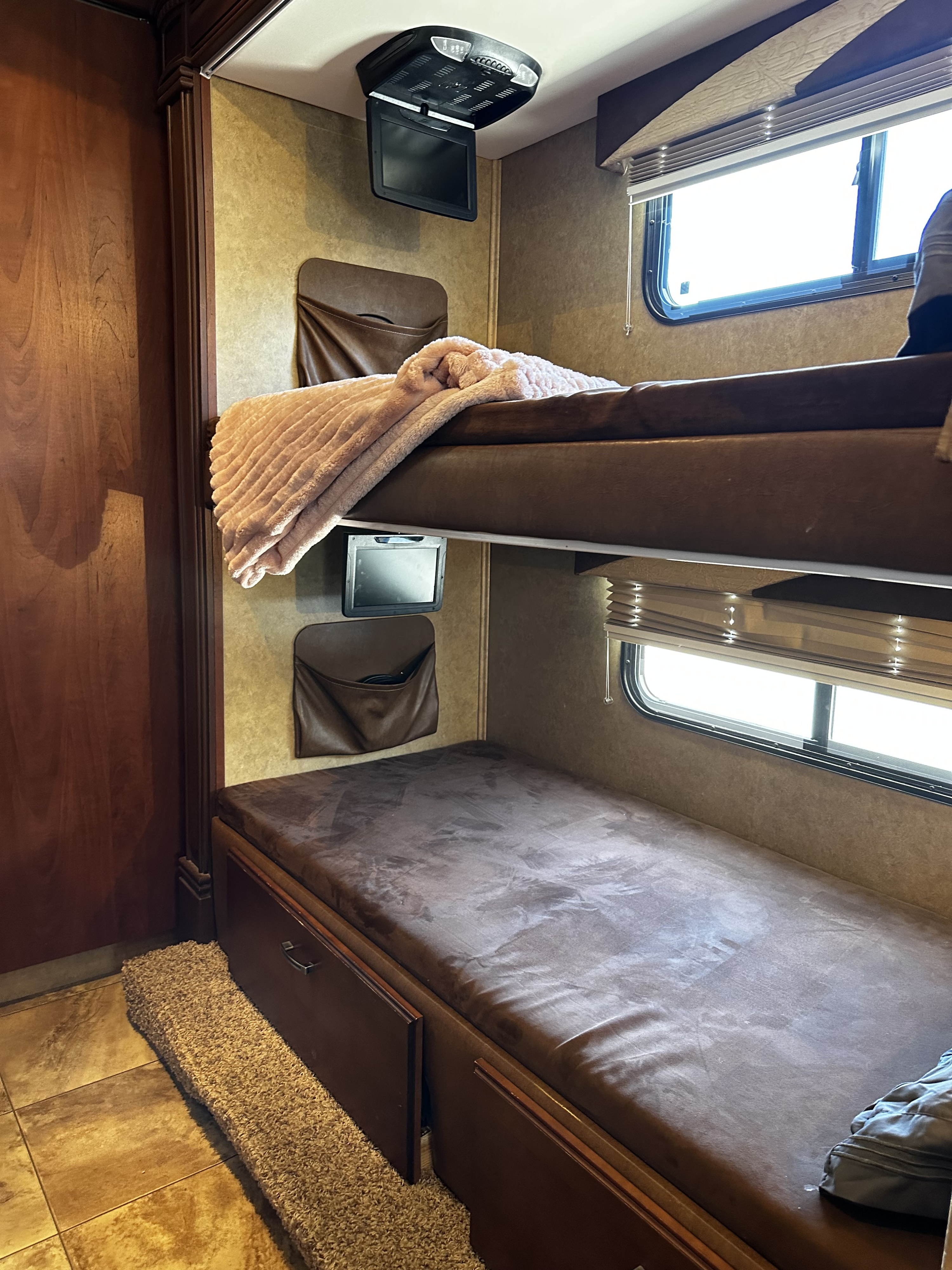 RV rental bunk room: upper and lower bunks with soft bedding, a ceiling-mounted TV, and wall storage pockets.. Jayco Greyhawk 2012