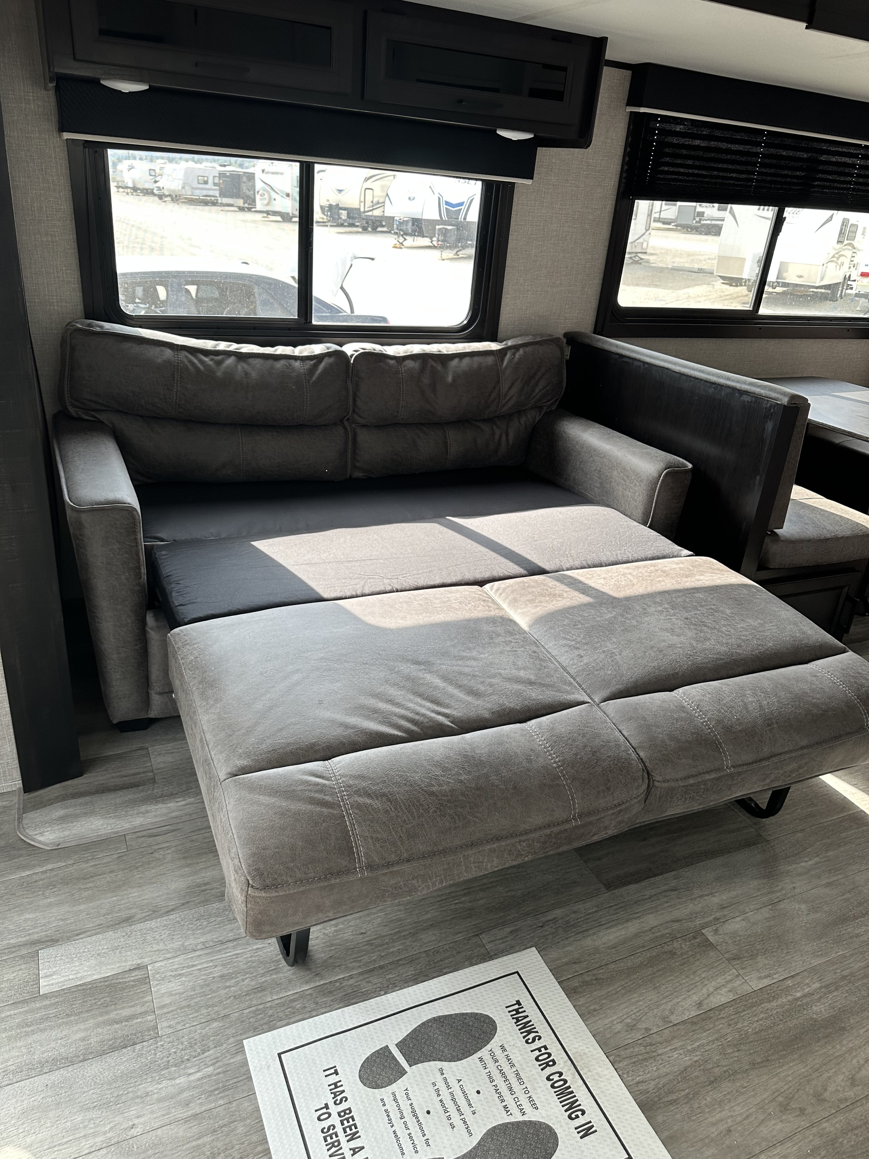 Grey sofa-bed pulled out in an RV rental, showing the dinette and other RVs outside on the lot.. Jayco Jay Flight SLX 2022