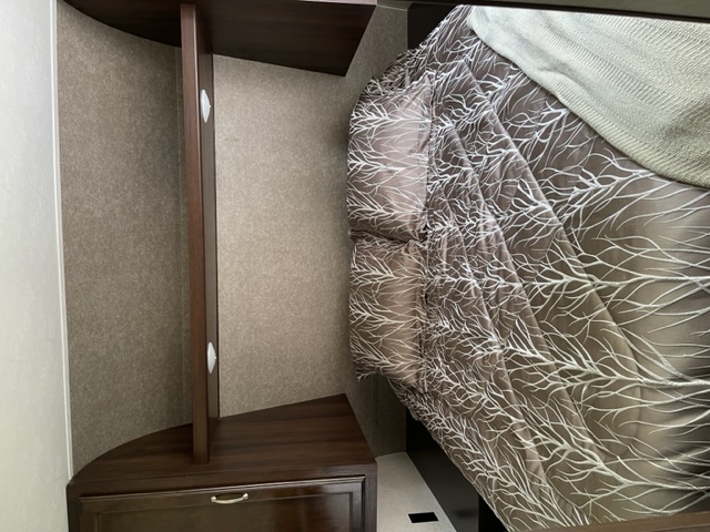 Cozy RV rental bedroom showing a bed with a tree-branch pattern comforter and adjacent curved storage cabinet with a drawer.. Jayco Jay Flight SLX 2018