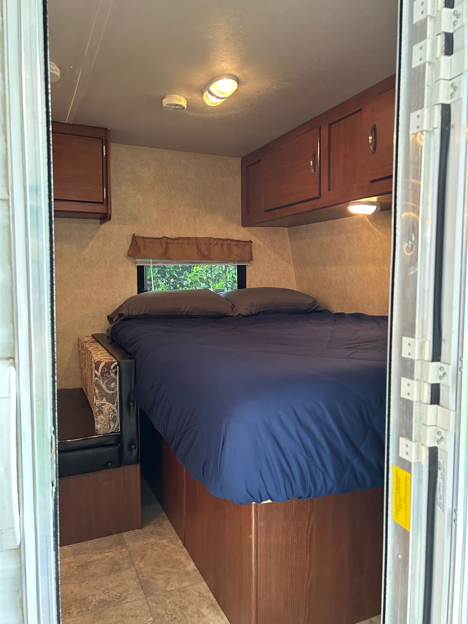 Inside an RV rental: a compact bedroom featuring a comfortable bed with blue bedding, overhead cabinets, and a window.. Forest River Wildwood X-Lite FS 2014