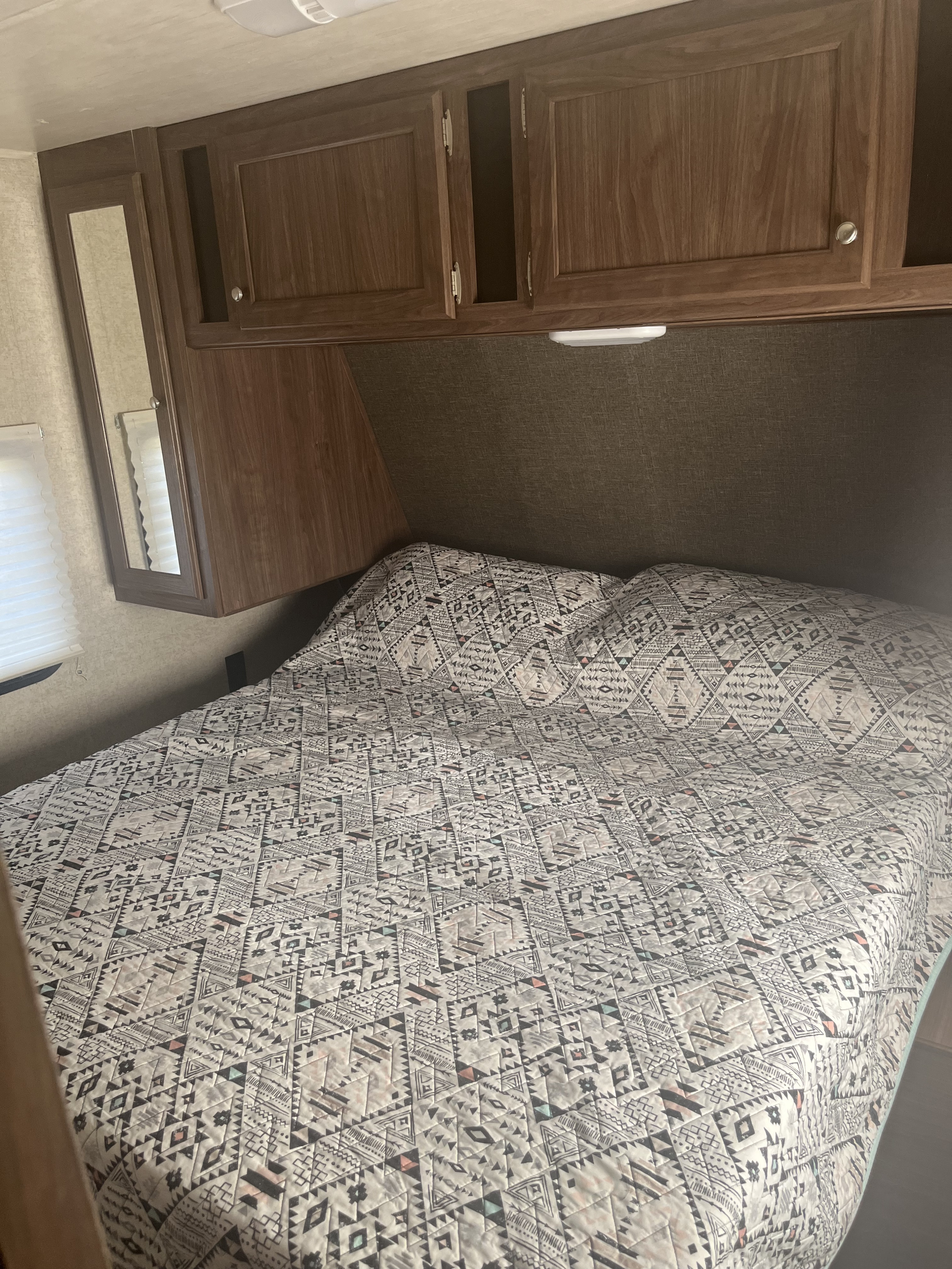 RV rental bedroom with patterned bed quilt, overhead cabinets (one open), and mirror door. Cozy camper interior.. Heartland RVs Pioneer 2018