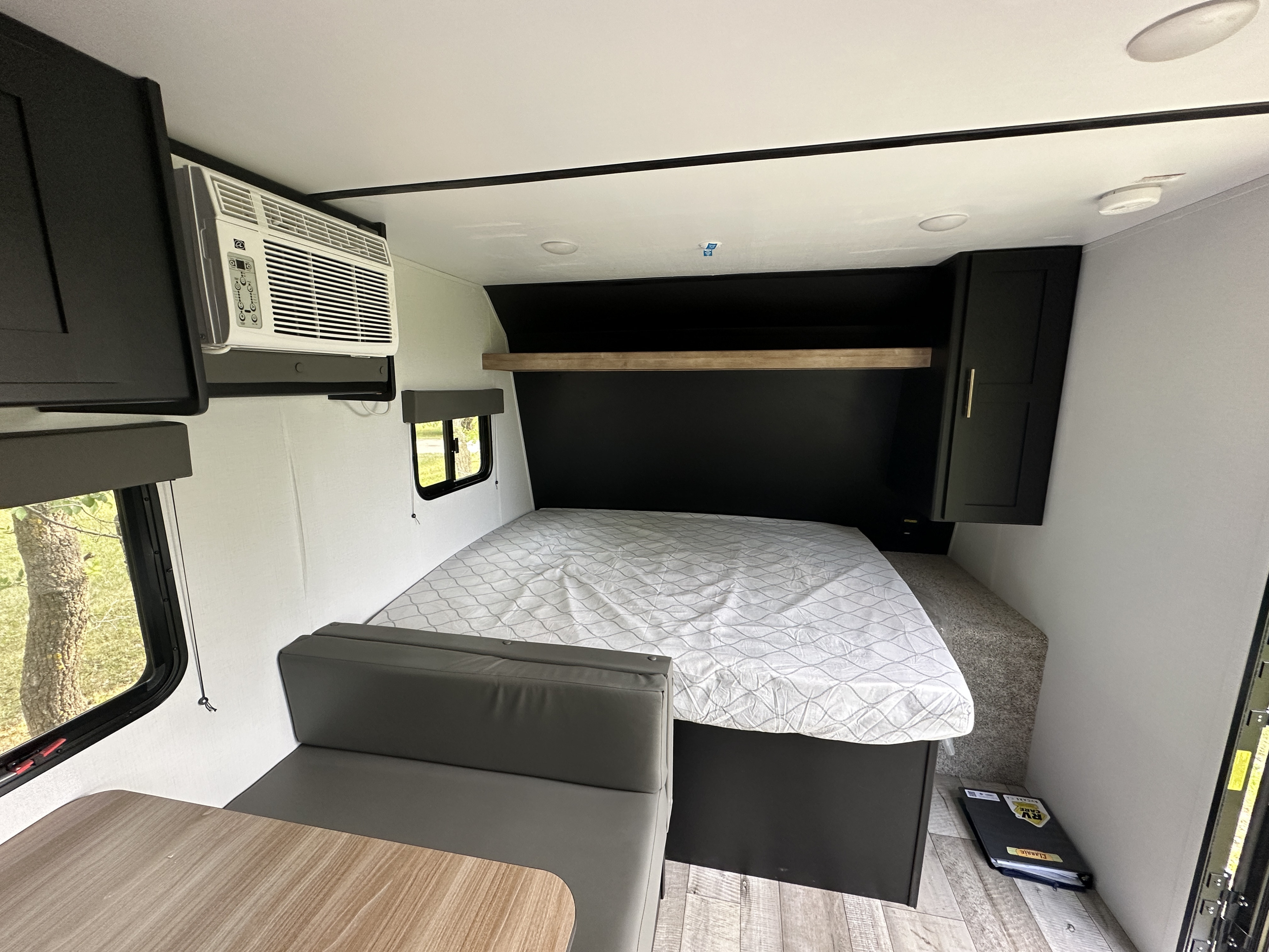 Cozy RV rental interior: featuring a comfy bed, grey dinette, AC unit, and overhead black storage cabinets.. Keystone RV Springdale 2022