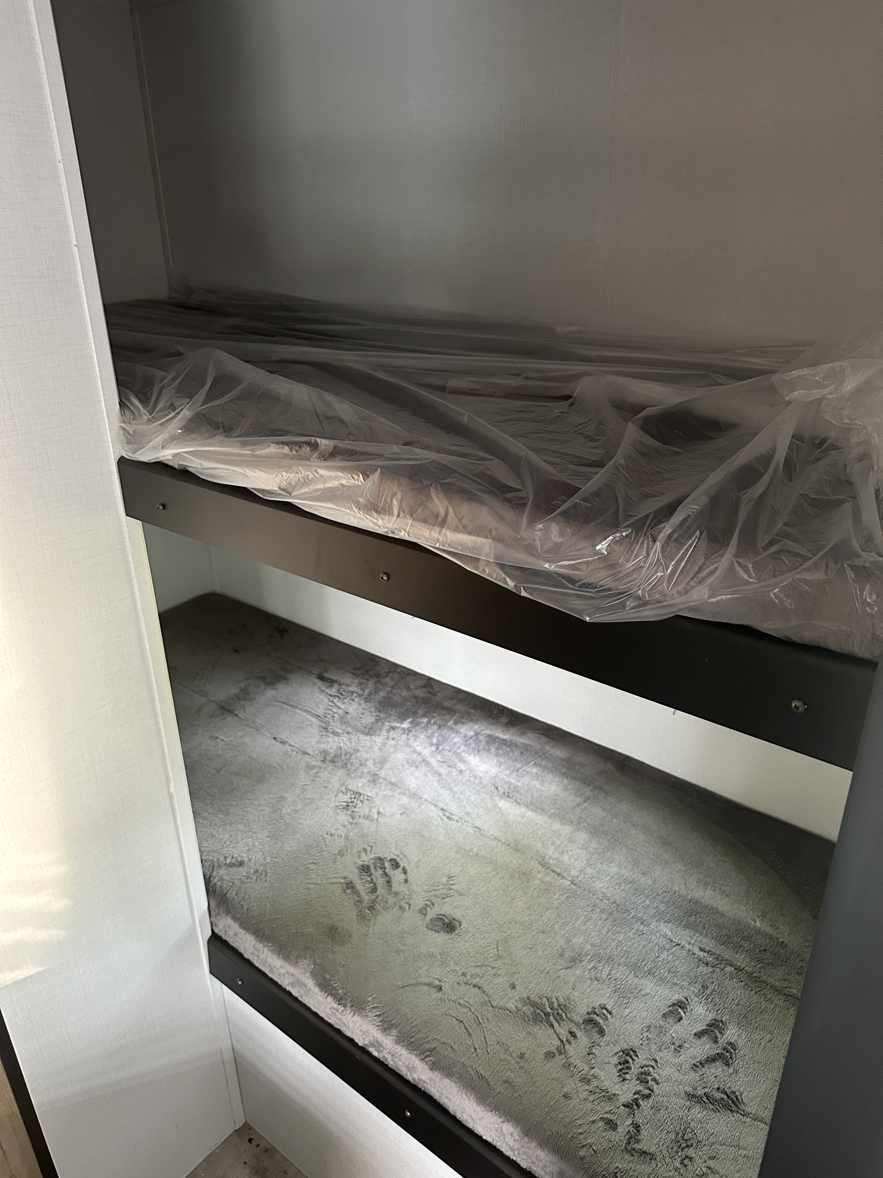 RV rental bunk beds: Top bunk mattress in plastic. Bottom bunk's soft gray surface has impressions.. Keystone RV Springdale 2022