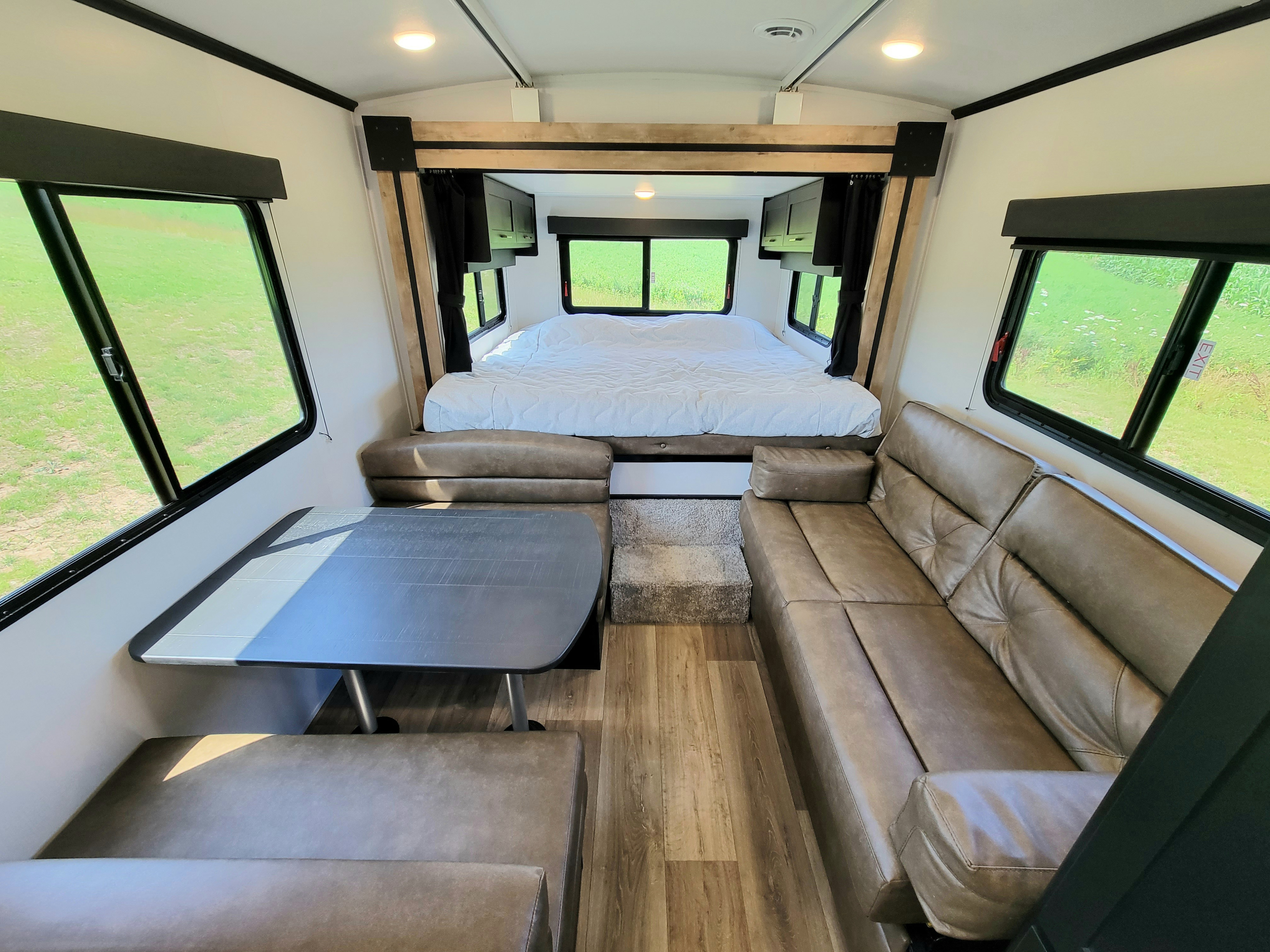 An inviting rv rental features a cozy bed, dining area, and sofa, with natural light from large windows.. Keystone Outback 2023