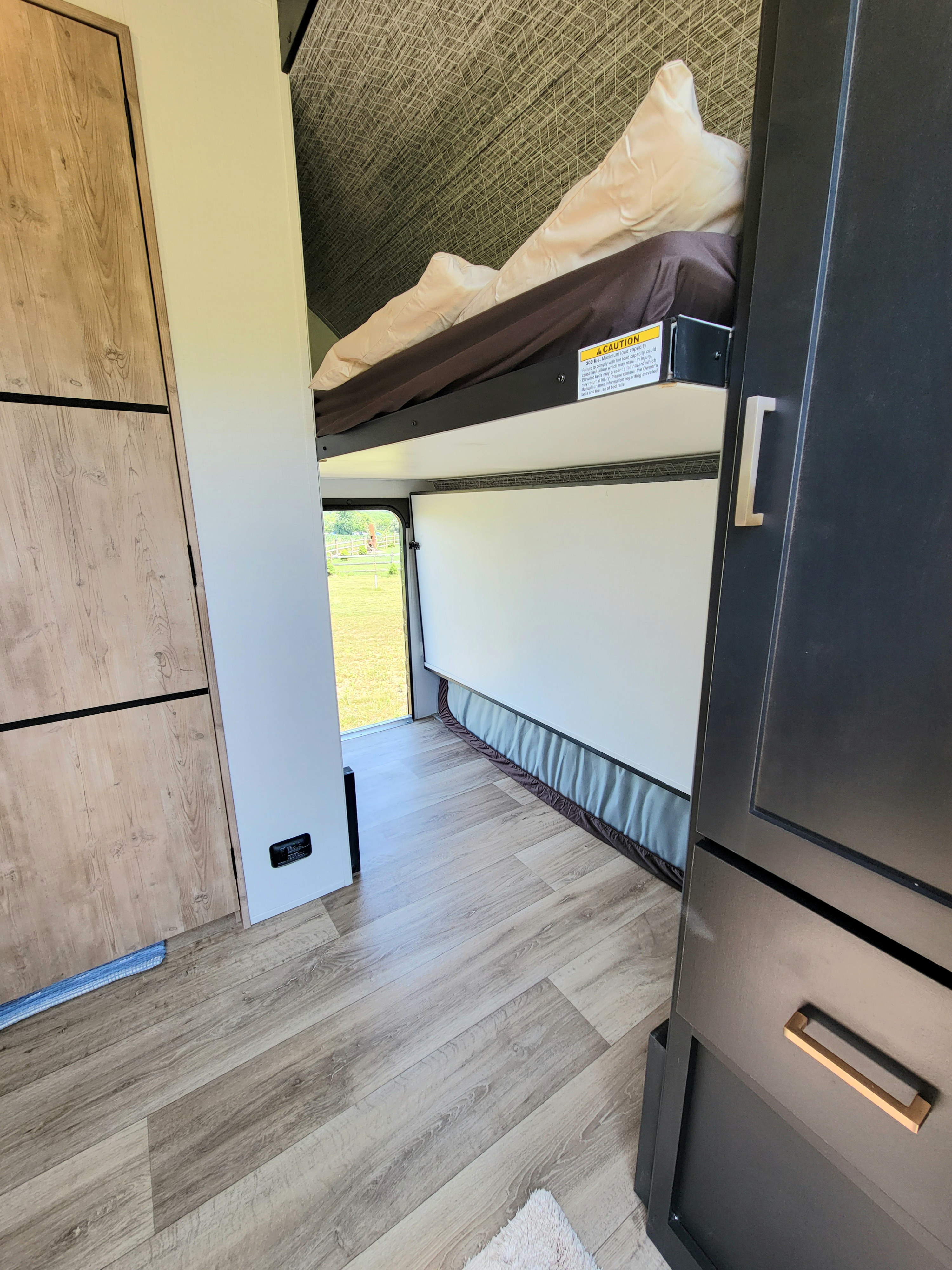 RV rental bunk beds: a compact and functional interior space with a safety warning for the upper bunk, perfect for travel.. Keystone Outback 2023