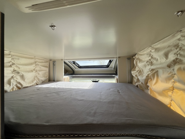 Cozy RV rental bedroom with spacious bed, light ceiling, ruffled curtains, and an overhead skylight view.. ITINEO PJ 700 2025