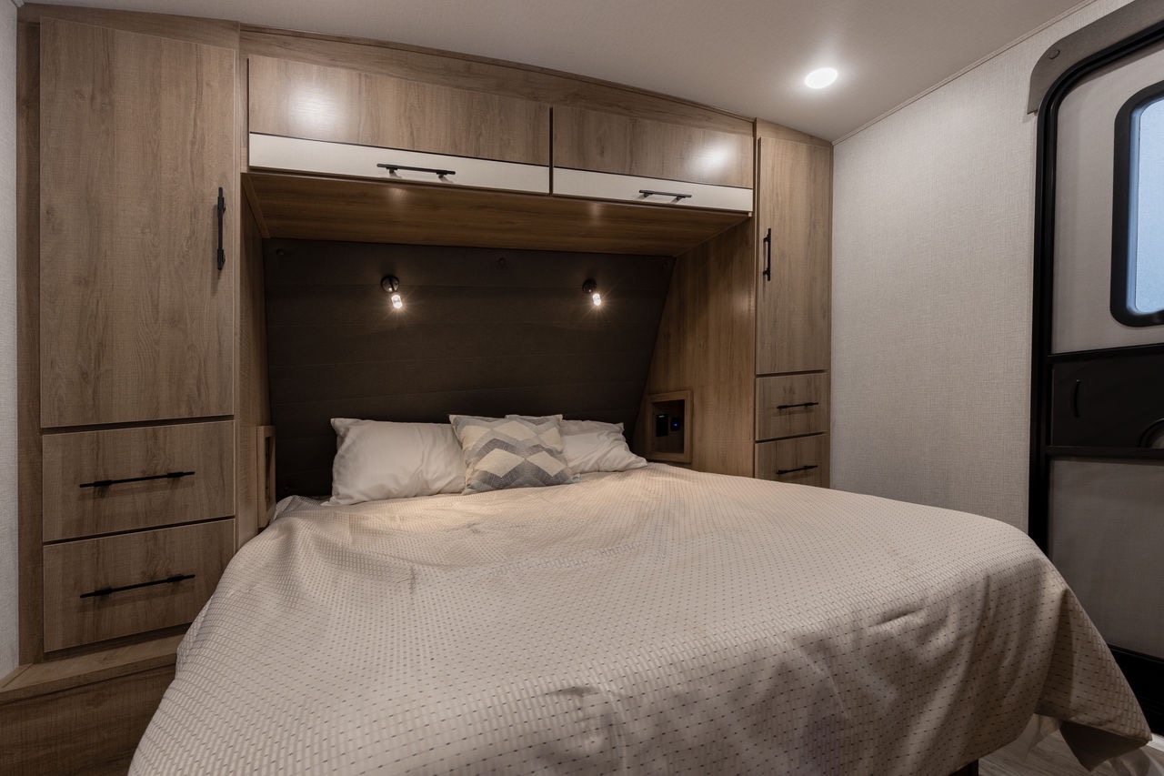 Cozy RV rental bedroom with warm wood cabinetry, built-in storage, and a comfortable bed.. Grand Design Imagine 2023