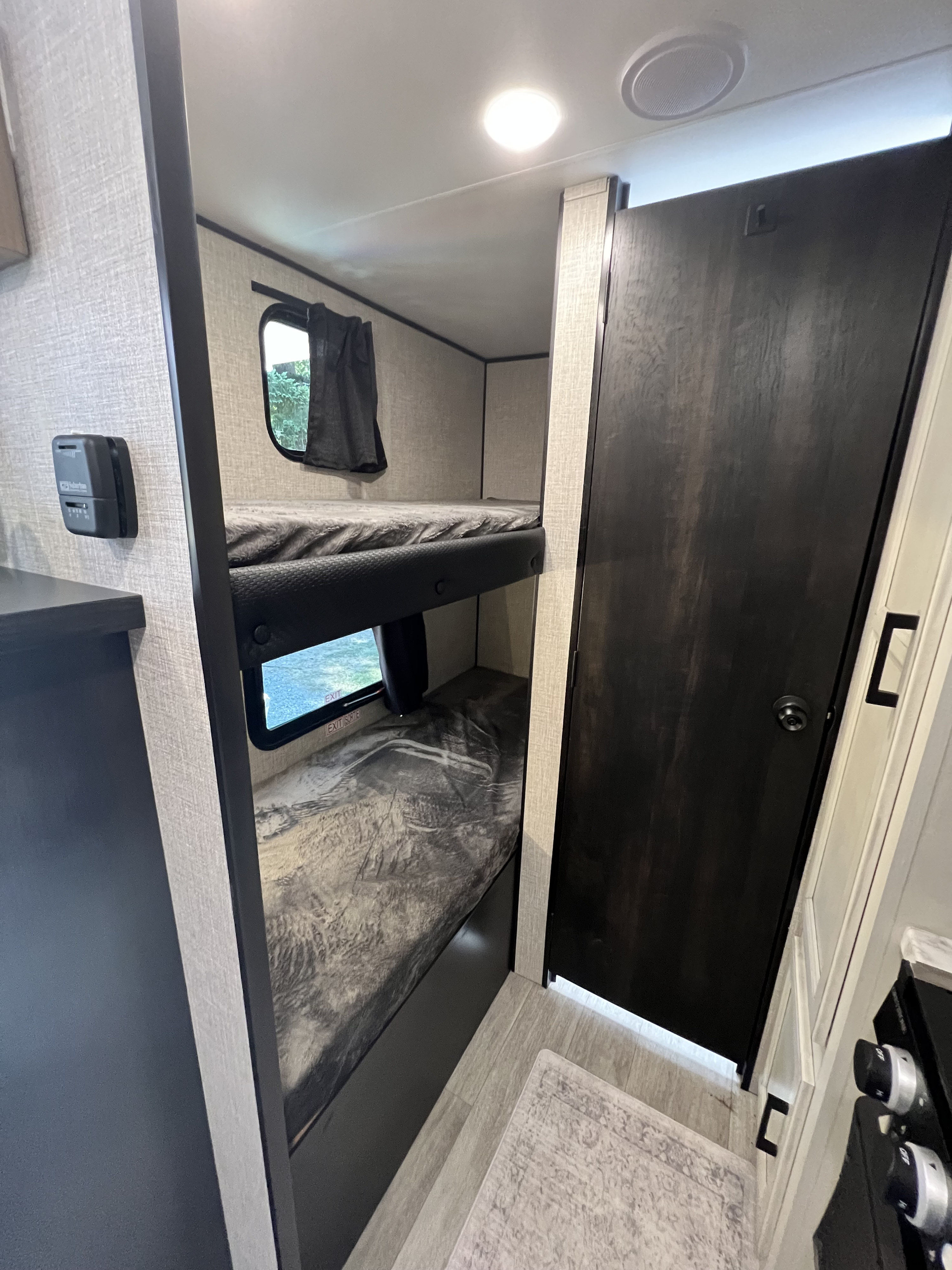 This RV rental features compact bunk beds and a dark door, offering efficient sleeping space in a travel trailer.. Jayco Jay Flight SLX Baja Edition 2023