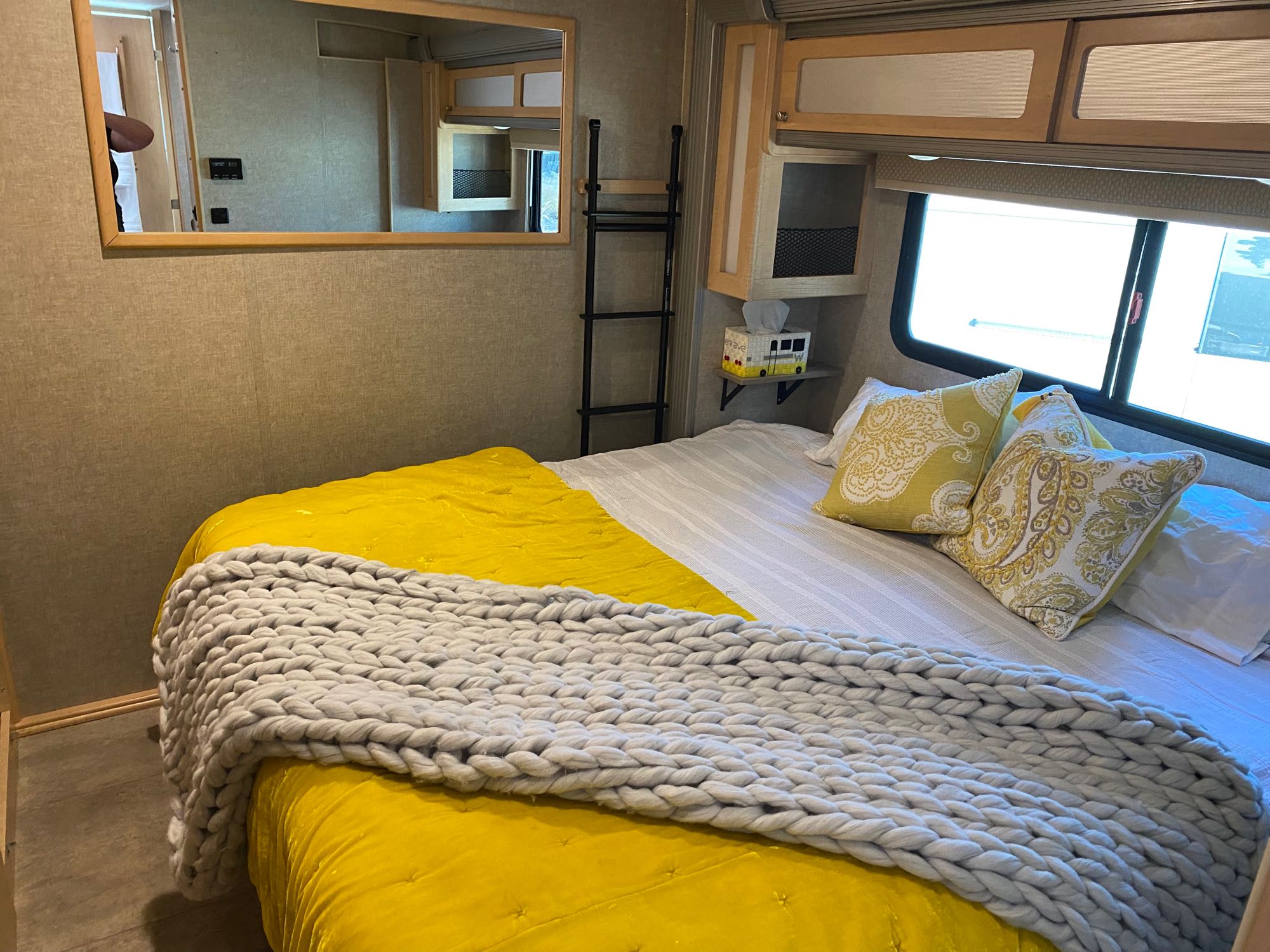 Cozy RV rental bedroom with vibrant yellow bedding, a chunky grey blanket, and mirrored wall adding depth.. Winnebago Brave 2016