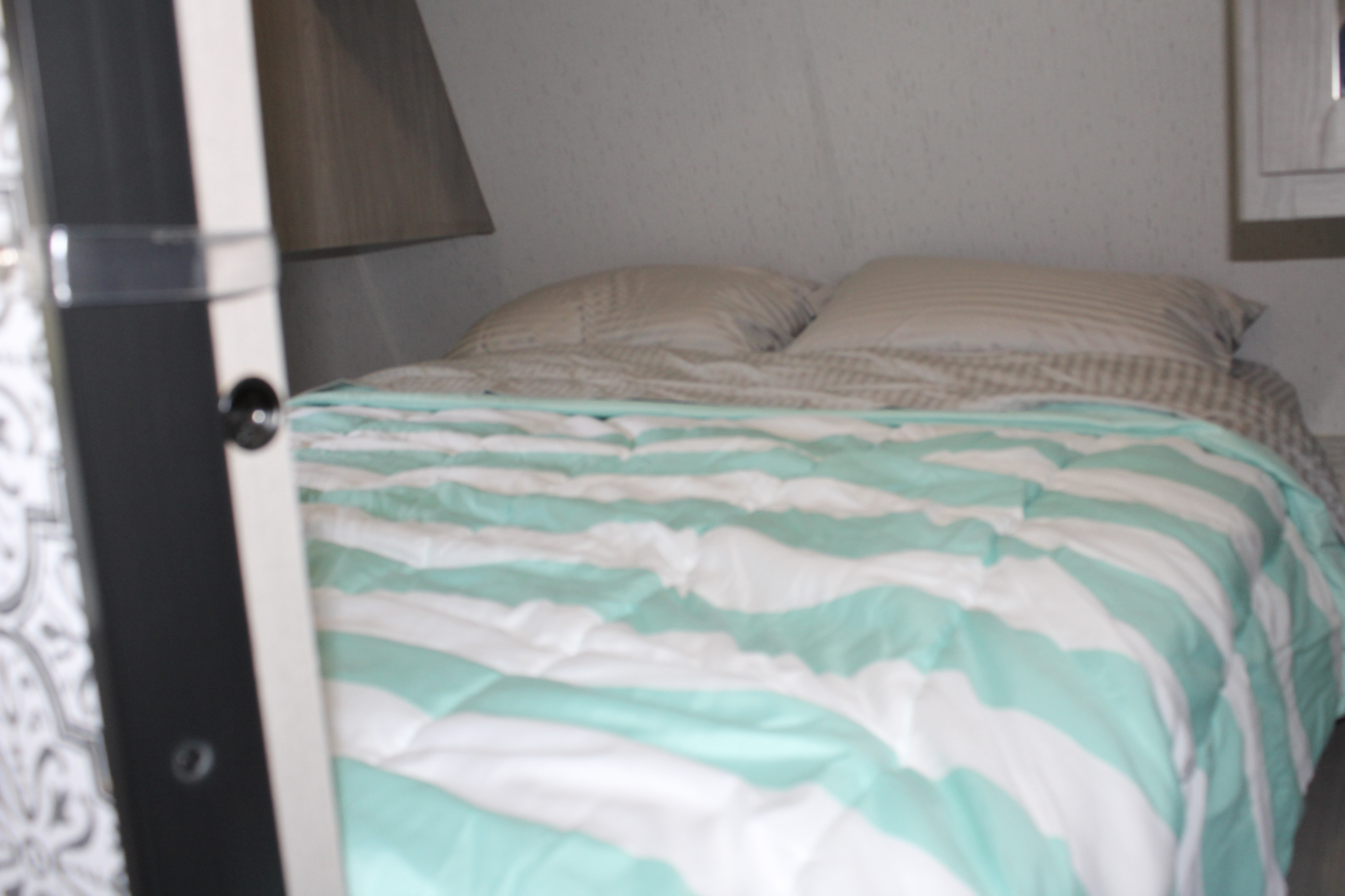 Cozy RV rental bedroom with a striped comforter and pillows, offering comfortable rest.. Dutchmen Coleman Lantern 2022