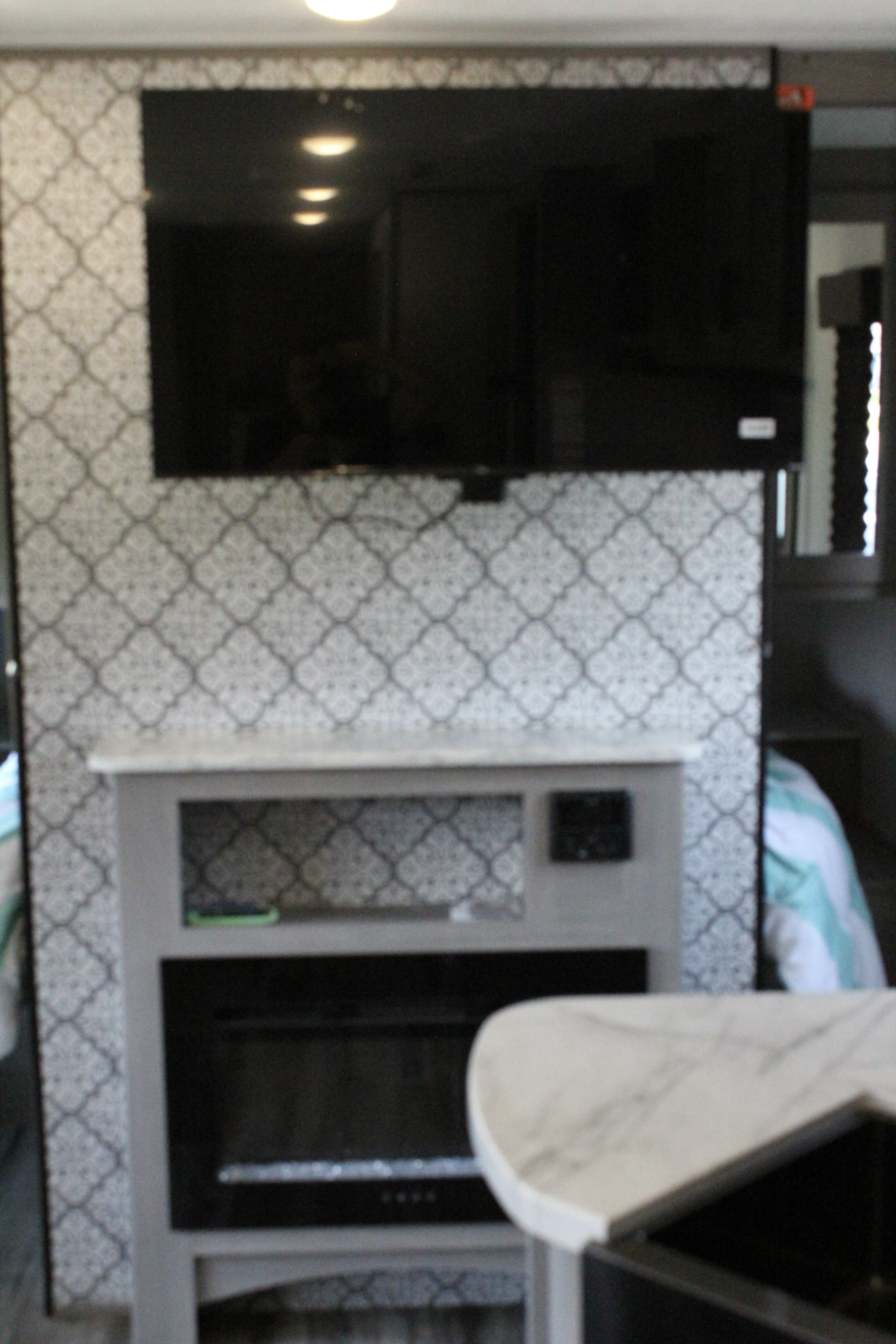 An RV rental's cozy living area with a wall-mounted TV above an electric fireplace, patterned wallpaper, and a counter.. Dutchmen Coleman Lantern 2022