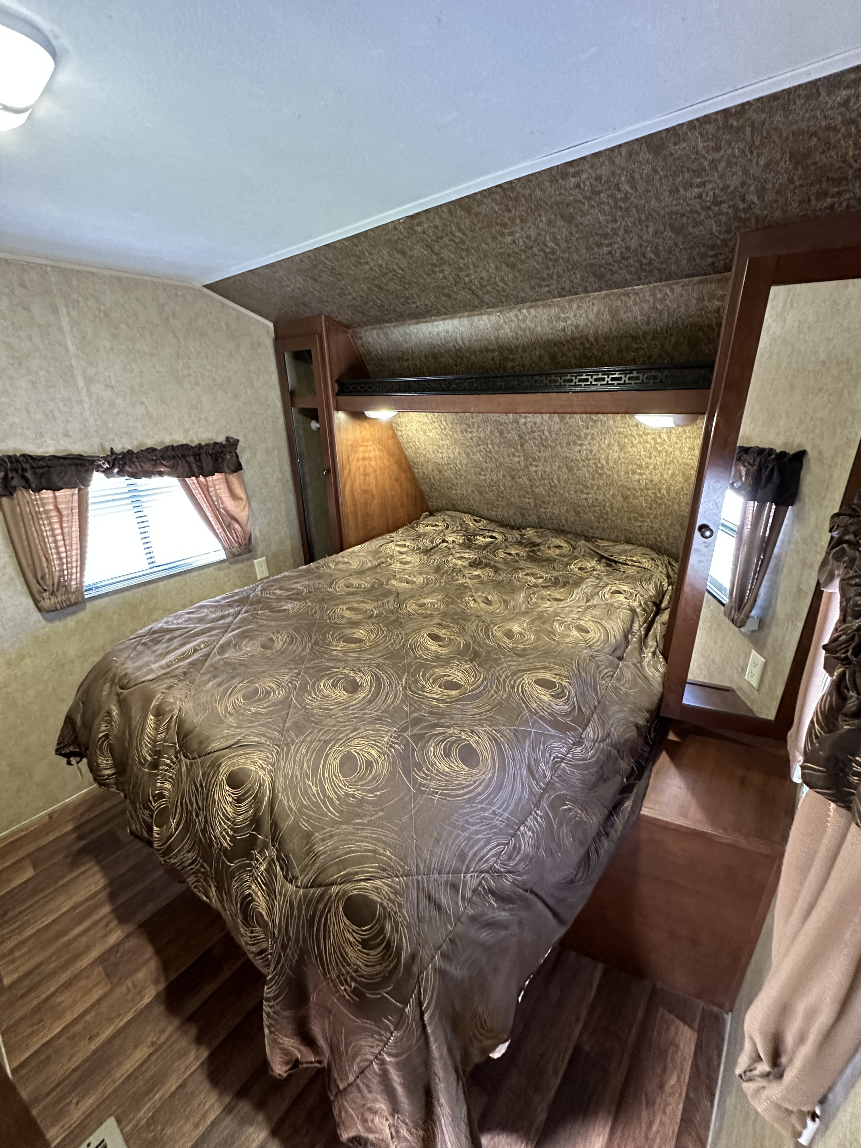 Cozy RV rental bedroom with a comfy bed, wood accents, and natural light from the window. Perfect for your next adventure.. Aspen Trail Aspen Trail Trailer 2013