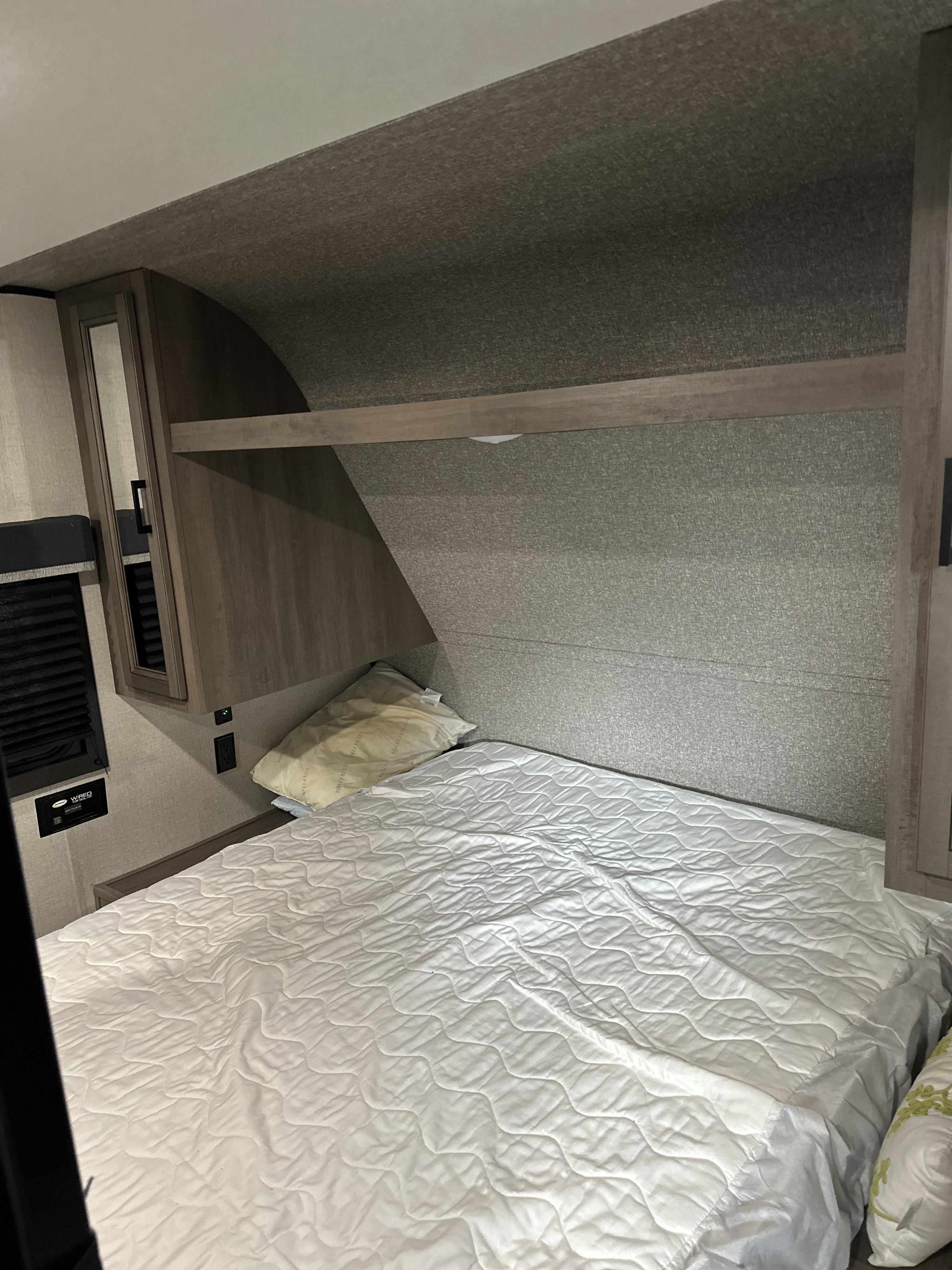 RV rental bedroom featuring a modern compact bed, quilted white bedding, and built-in wood cabinetry for storage.. Highland Ridge RV Open Range 2022