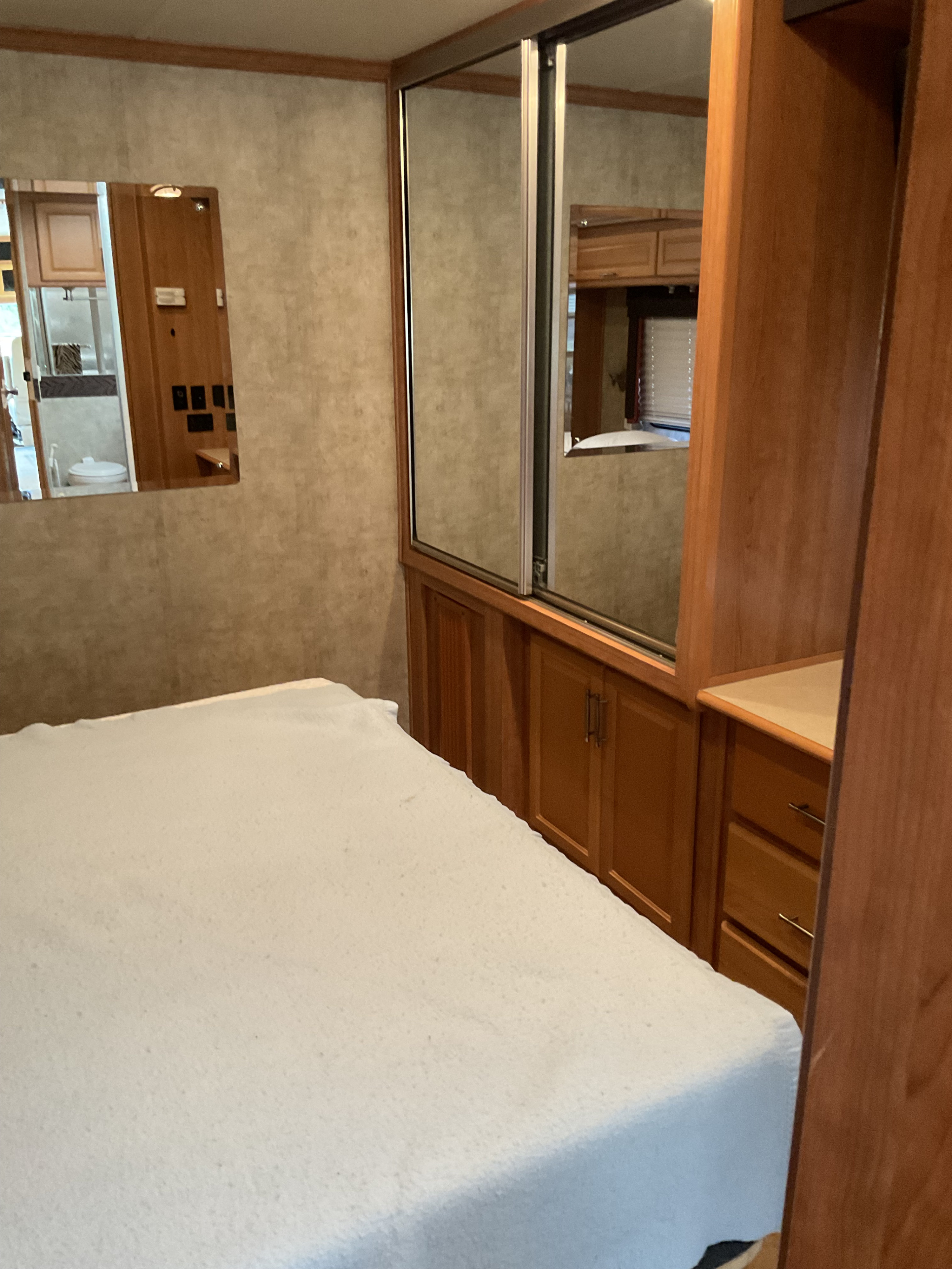 RV rental bedroom showing a white bed, mirrored sliding closet, wood storage drawers, and bathroom reflection.. Fleetwood Southwind 2009