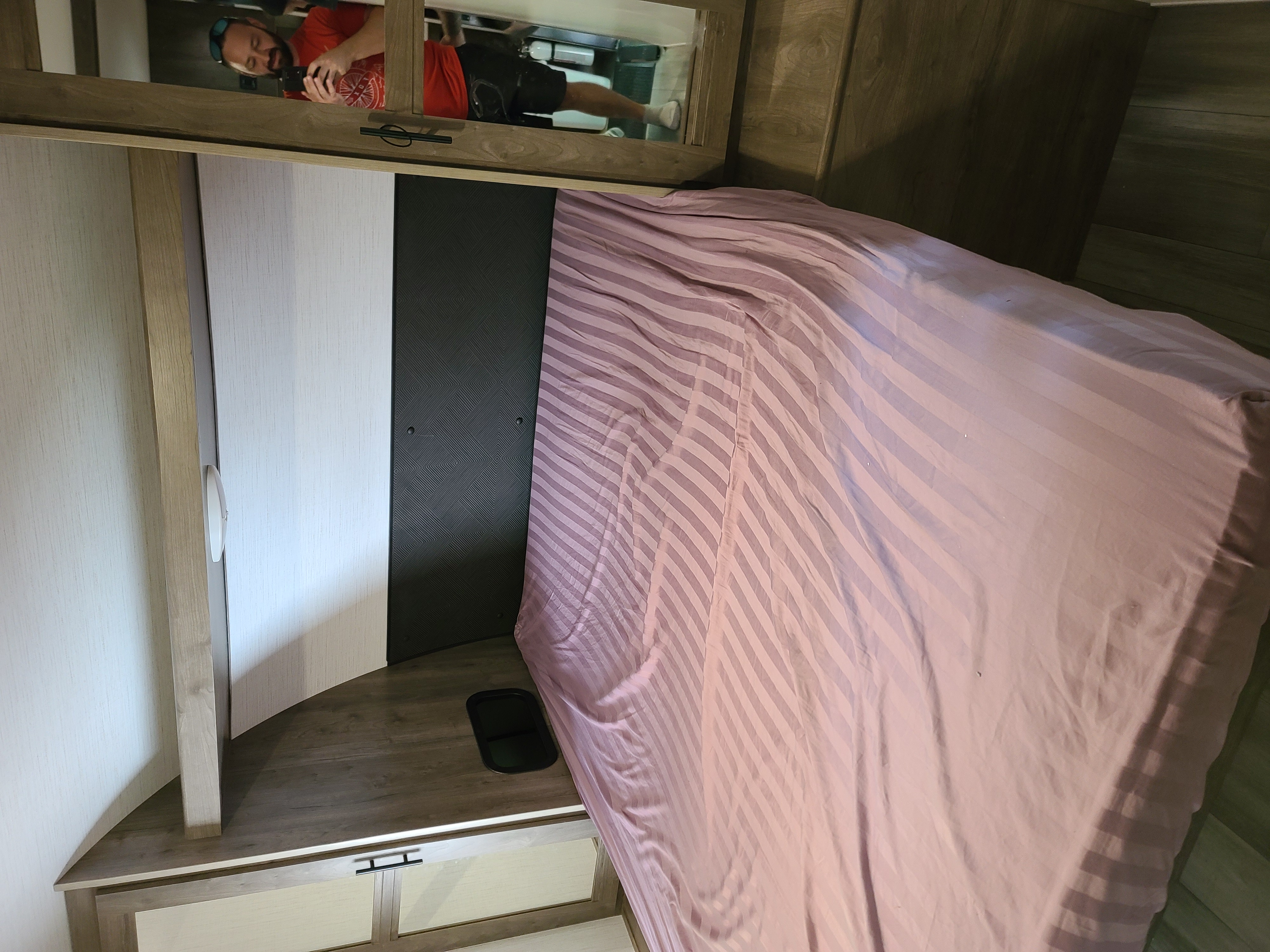 **RV rental** bedroom showing a pink striped bed and mirror reflecting a person capturing the scene.. Heartland RVs Pioneer bh270 2022