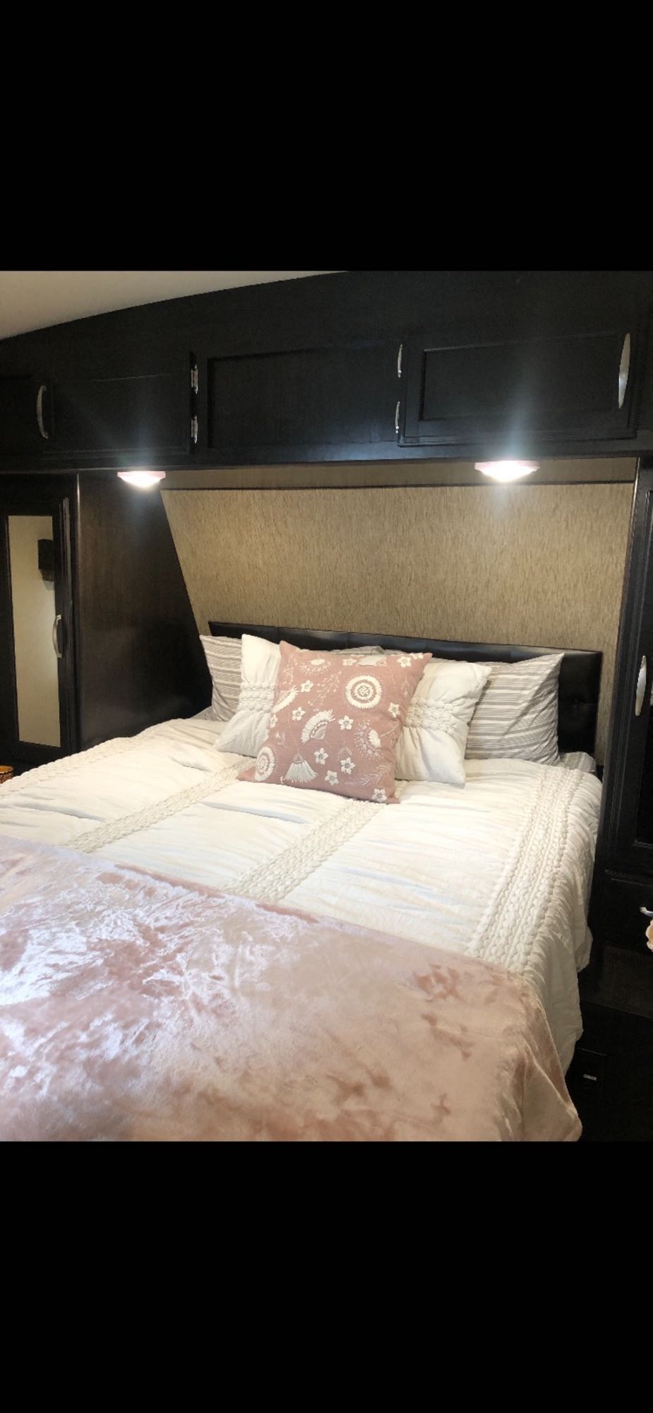 Relaxing RV rental bedroom featuring soft white bedding, a pink throw, and convenient overhead storage.. Grand Design Imagine 2017