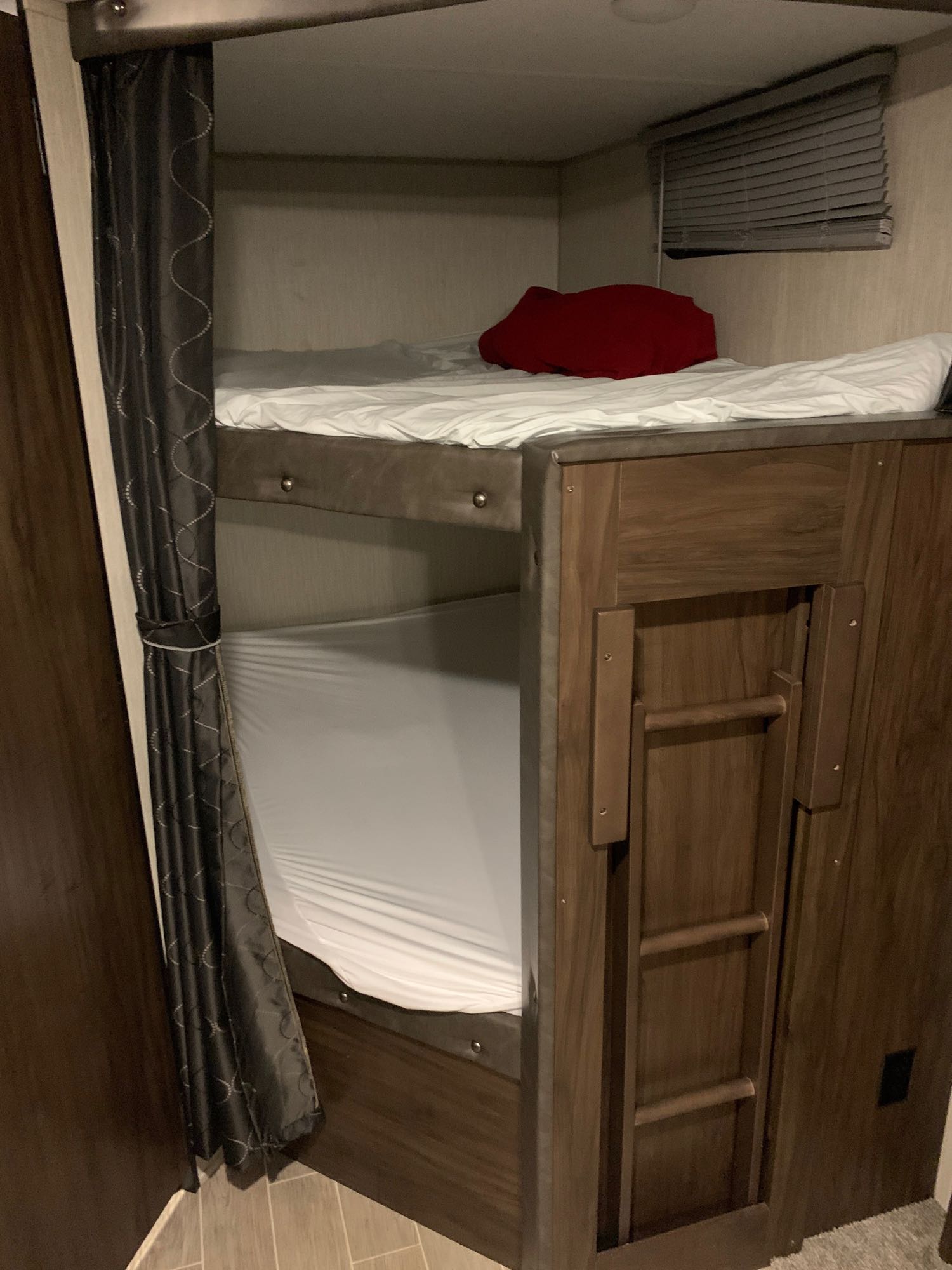 Cozy bunk beds in an RV rental interior, featuring white sheets, a red pillow, curtains, and an integrated ladder for access.. Forest River Cherokee Grey Wolf 2020