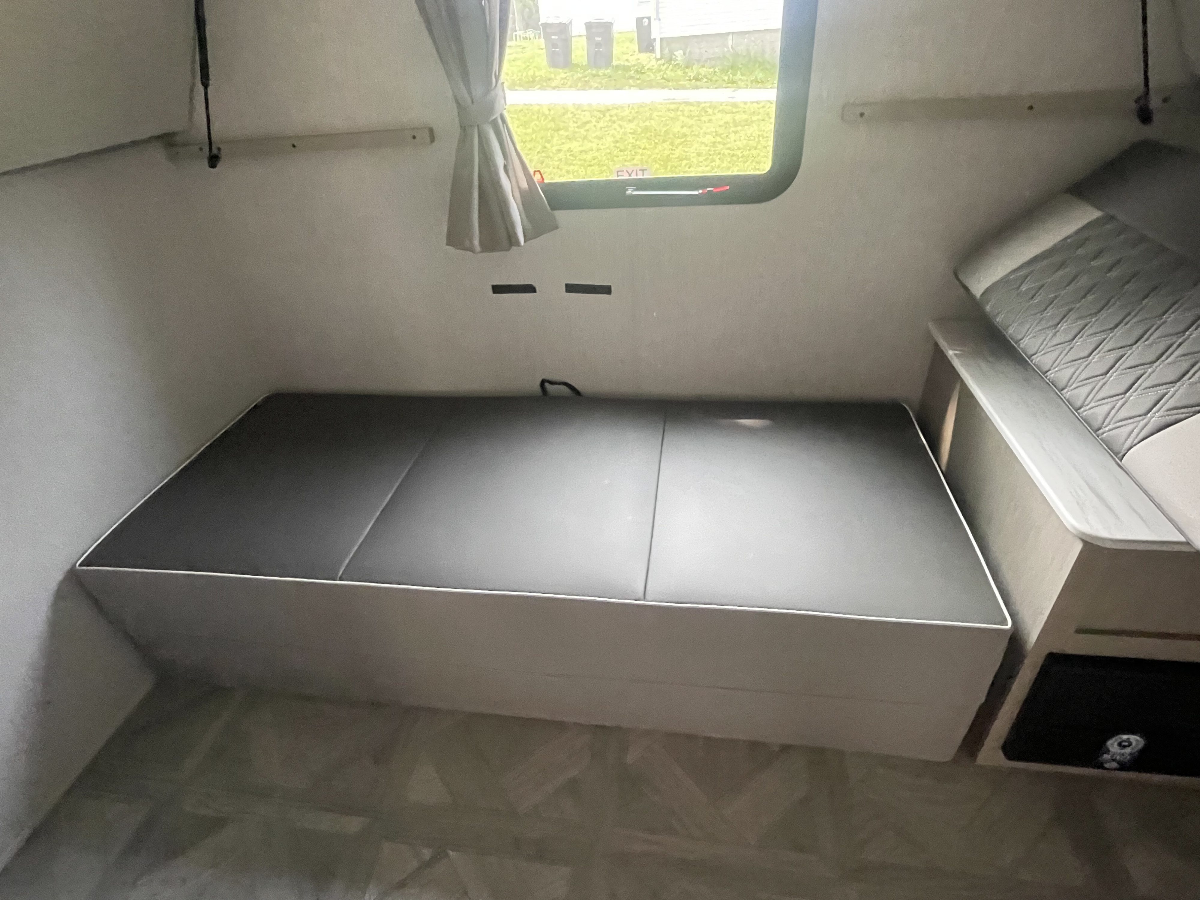 RV rental interior: a compact, functional space with a gray convertible sleeping/seating area and an adjacent window.. Forest River Wildwood X-Lite Platinum 2023