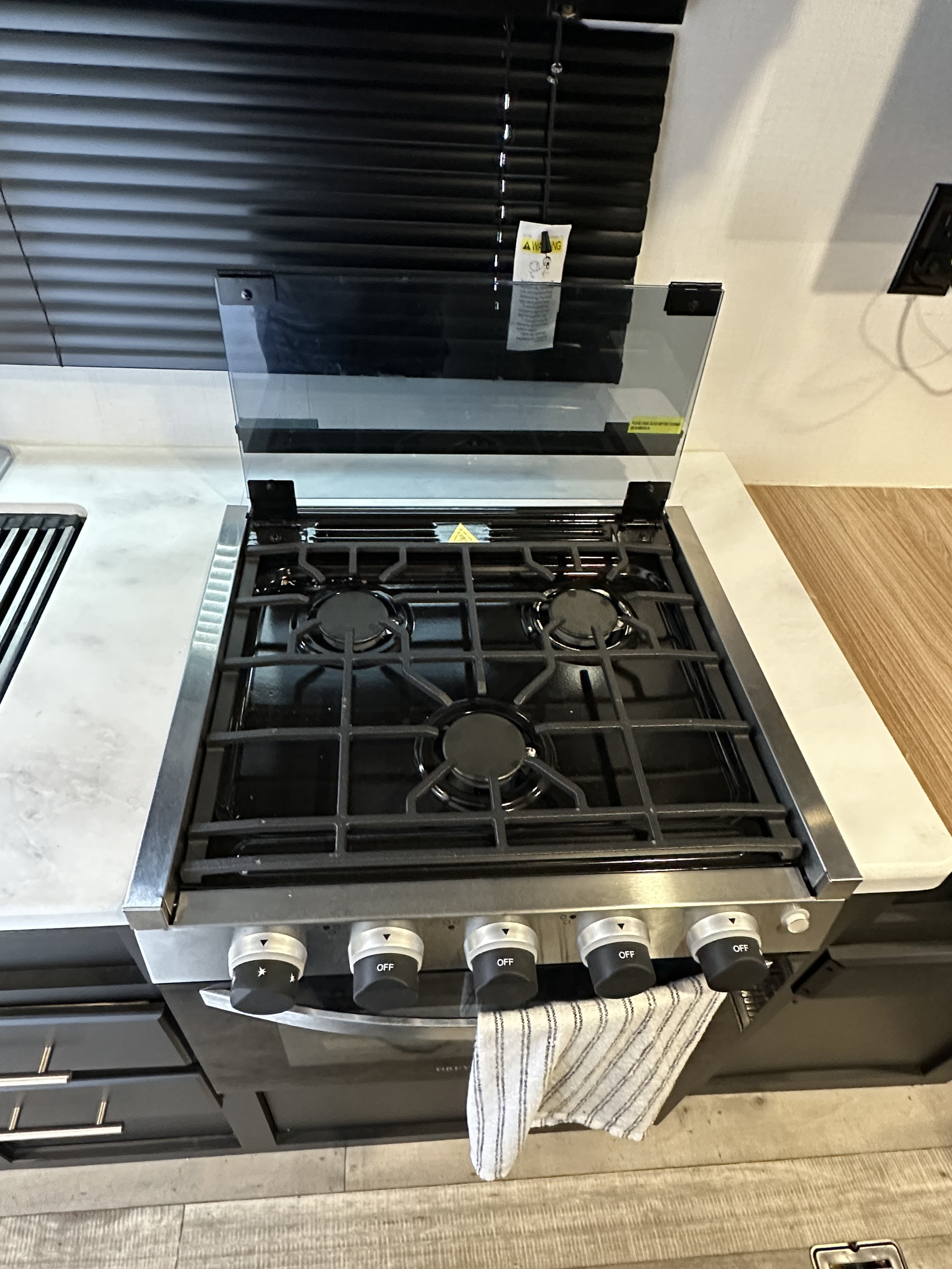 This RV rental kitchen features a clean, stainless steel gas cooktop with four burners, a glass lid, and control knobs.. Keystone RV Springdale 2022