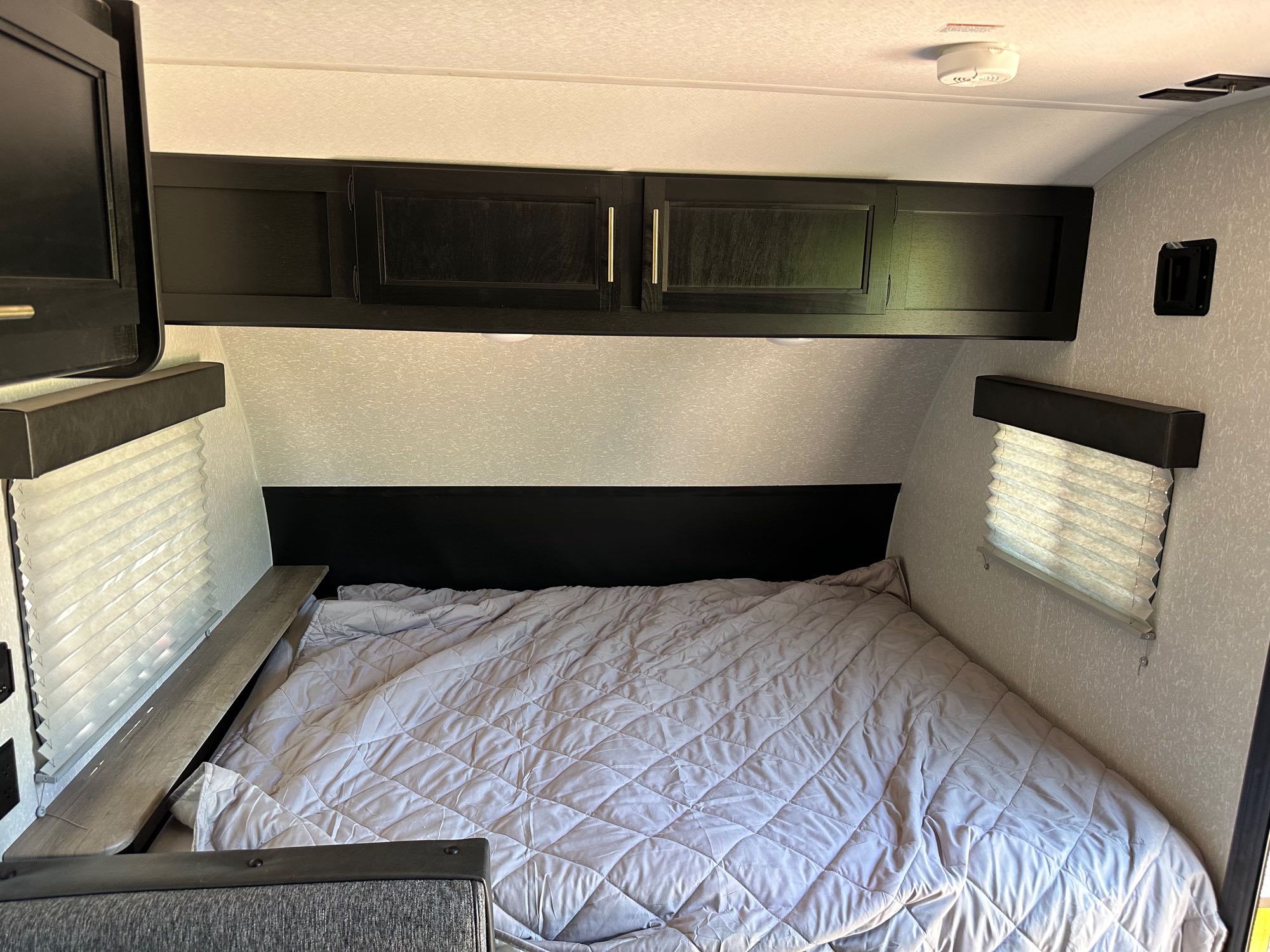 Cozy RV rental bedroom with a quilted bed, overhead storage cabinets, and window blinds. Ideal for an adventure.. Forest River Cherokee Wolf Pup 2022