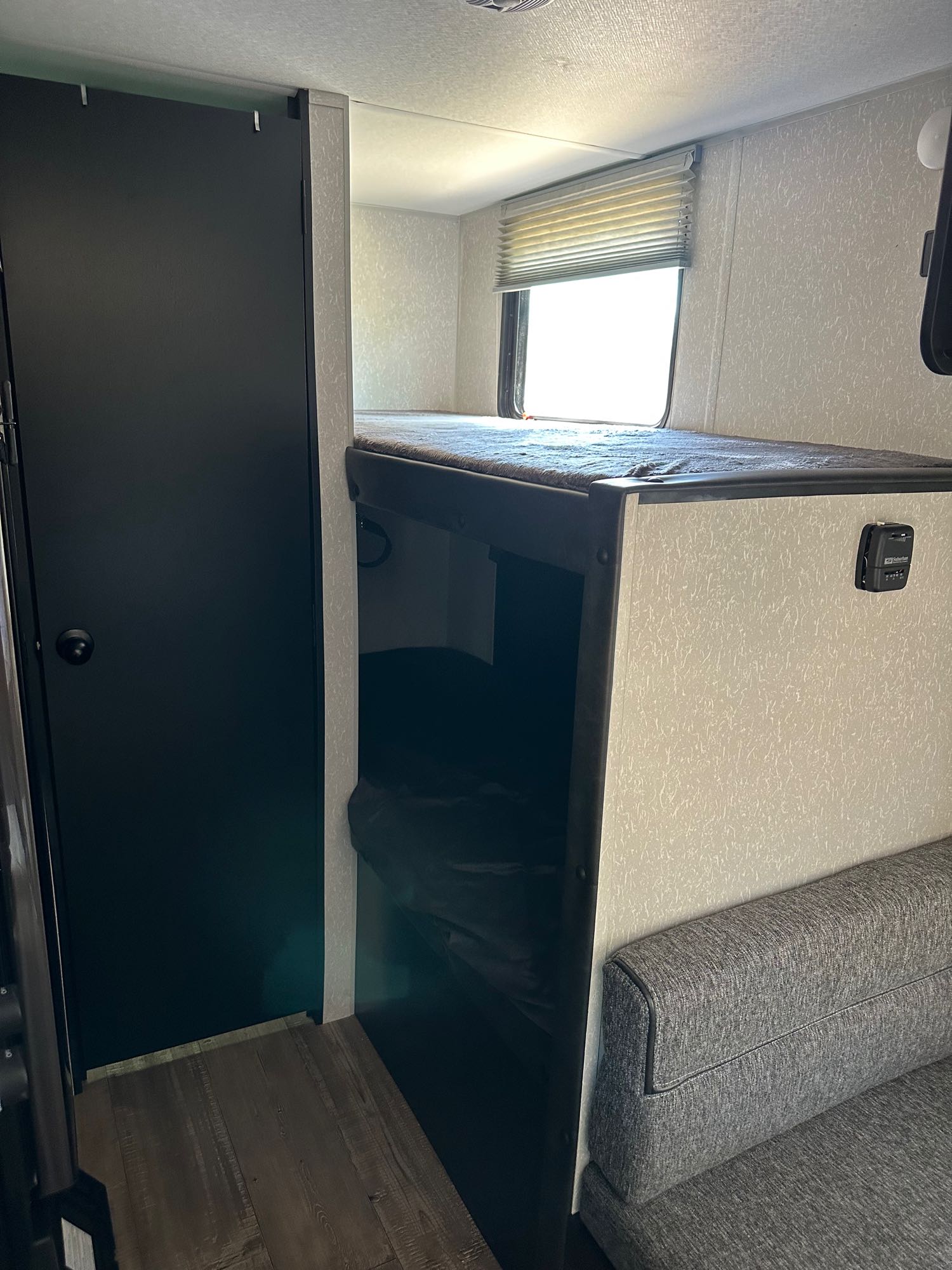 RV rental interior: A compact space featuring dark upper and lower bunk beds, a black door, and a comfy gray sofa.. Forest River Cherokee Wolf Pup 2022