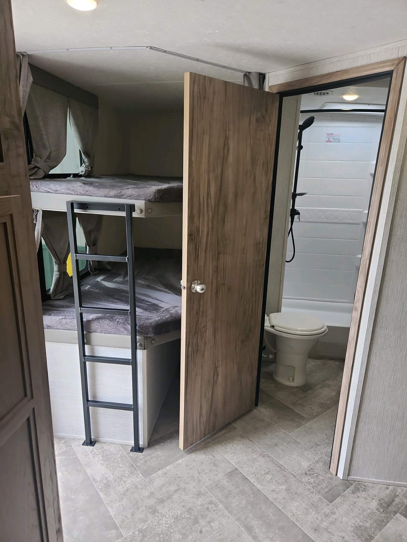 RV rental interior featuring cozy bunk beds with ladder and an adjacent compact bathroom with toilet and shower.. Palomino Solaire 2022