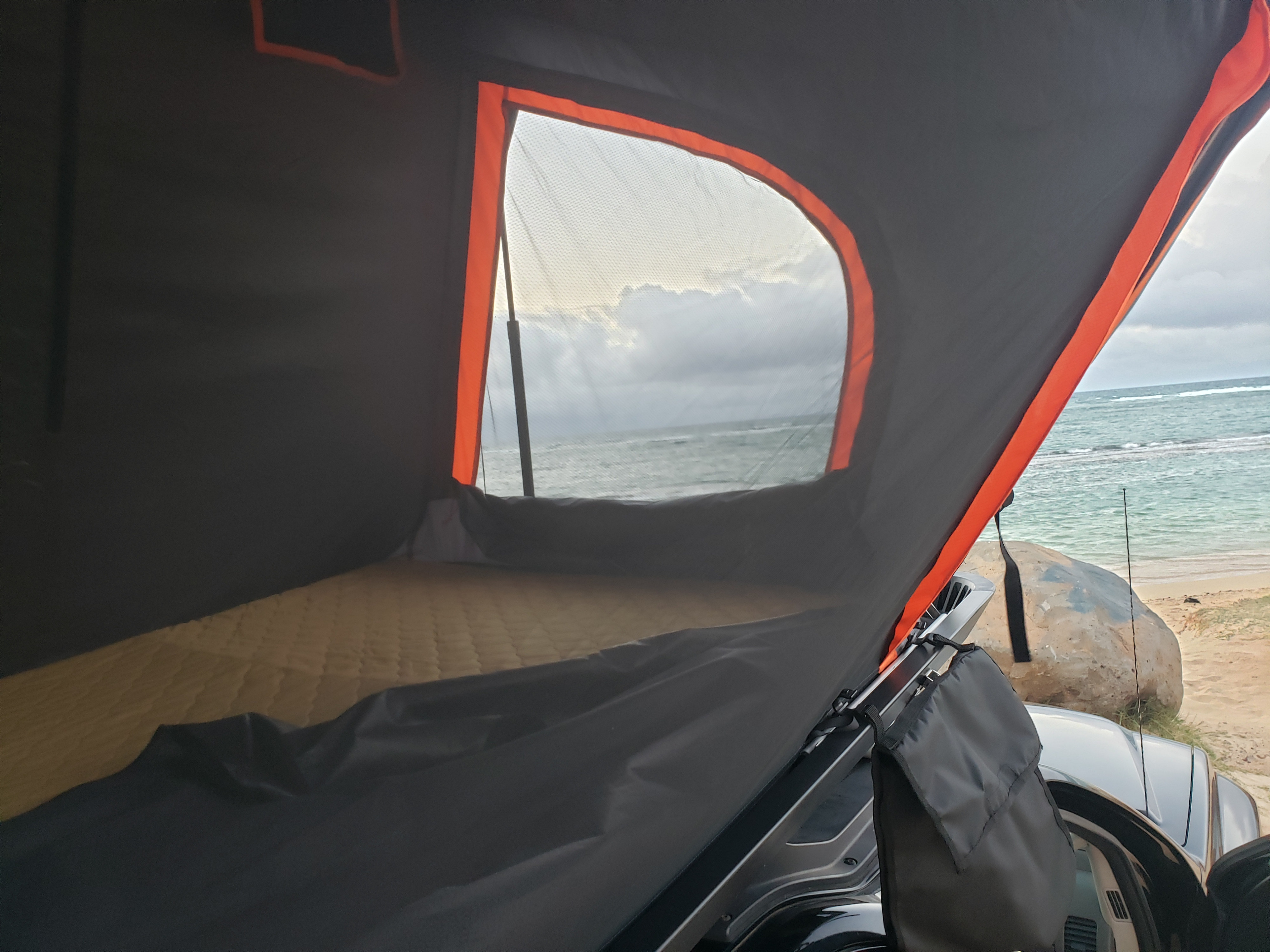 Inside a rooftop tent by the ocean, showing a mattress & beach view. Ideal for your next RV rental escape.. Nissan Xterra 2012