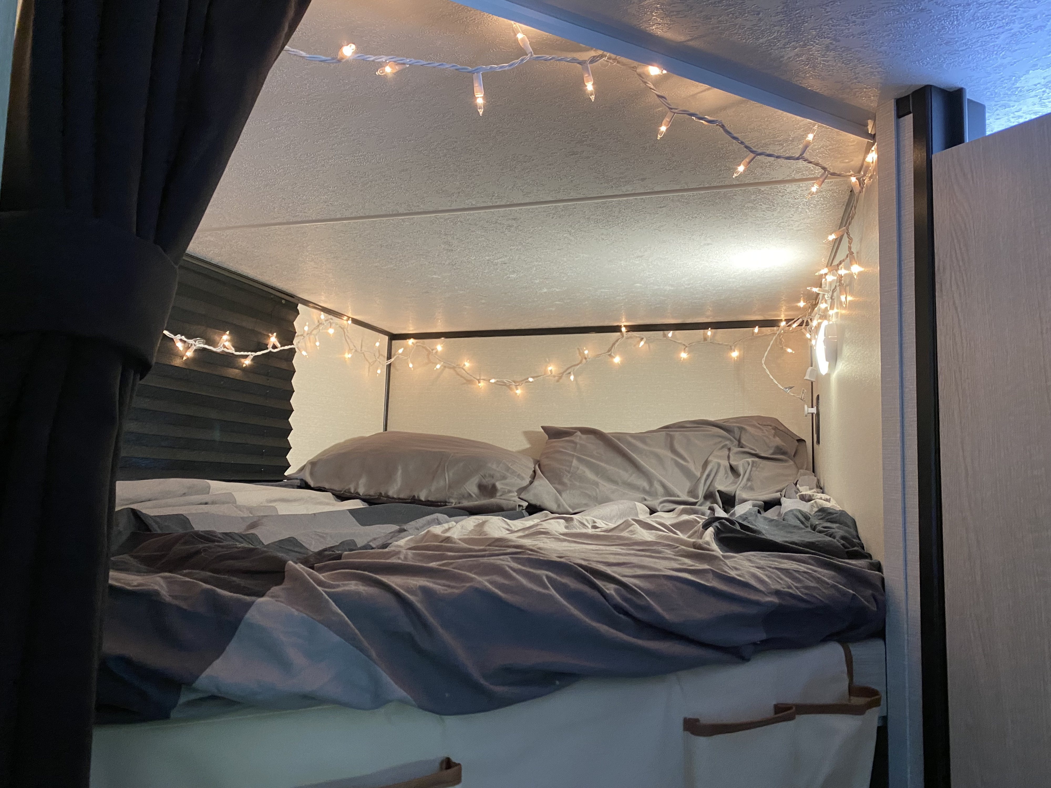 Cozy bunk bed inside an RV rental, illuminated by warm string lights, offering a comfortable and inviting sleeping area.. Coachmen Apex 2023