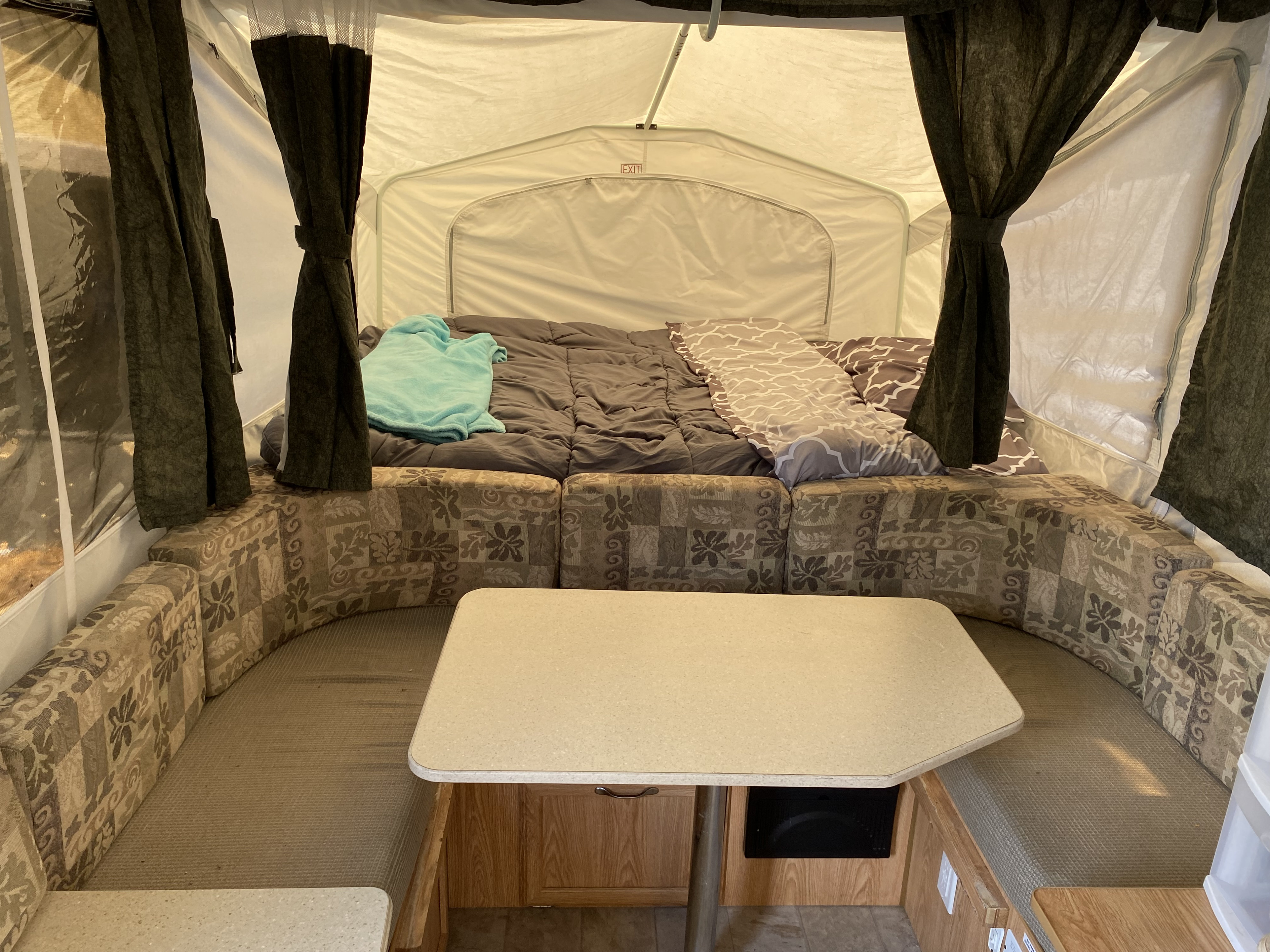 Interior view of an rv rental pop-up camper, showing the bed and dinette area with patterned cushions and a table.. Palomino Yearling 2012