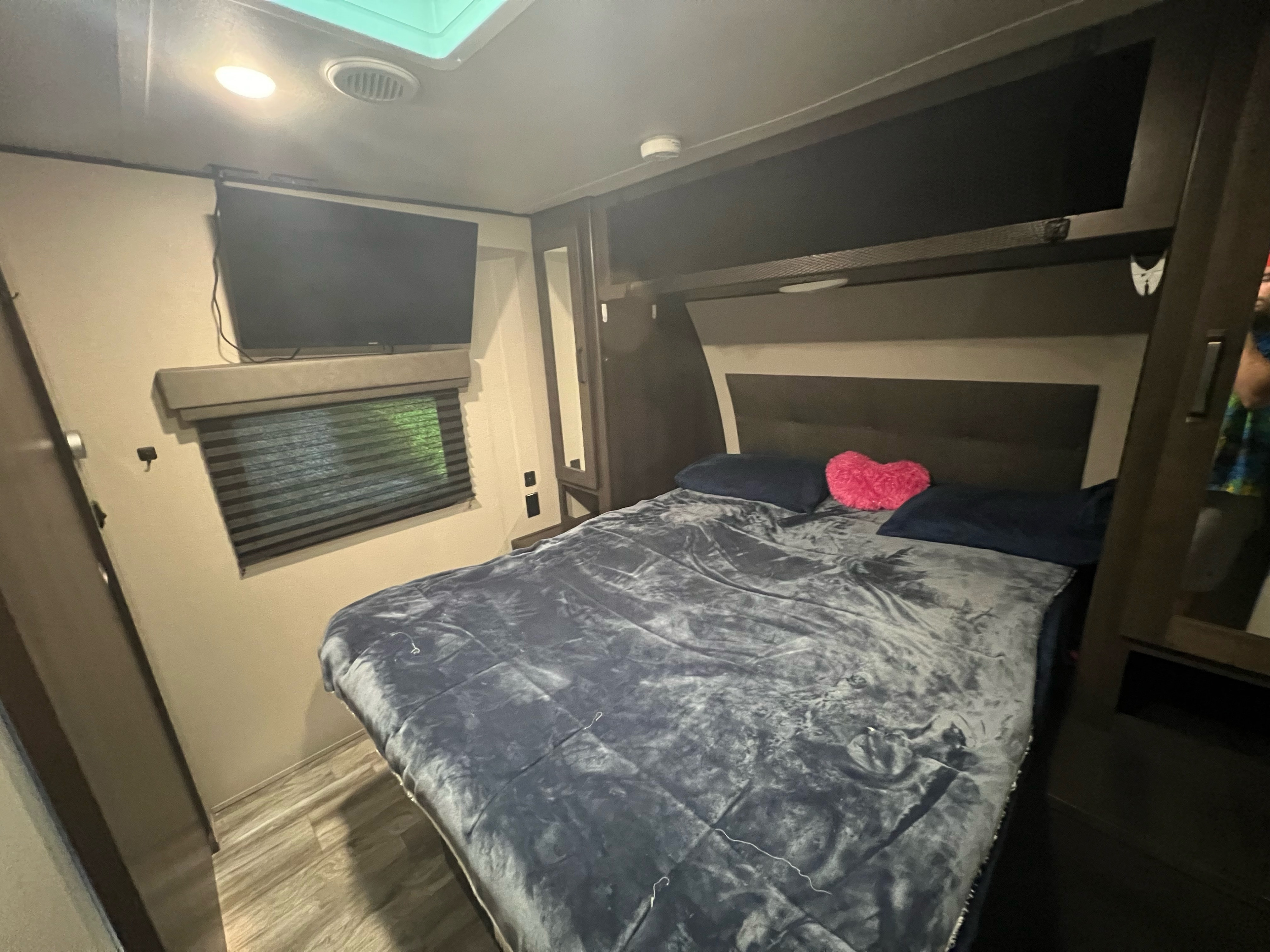 Cozy RV rental bedroom featuring a comfortable bed, wall-mounted TV, window, and useful overhead storage.. Grand Design Transcend Xplor 2022