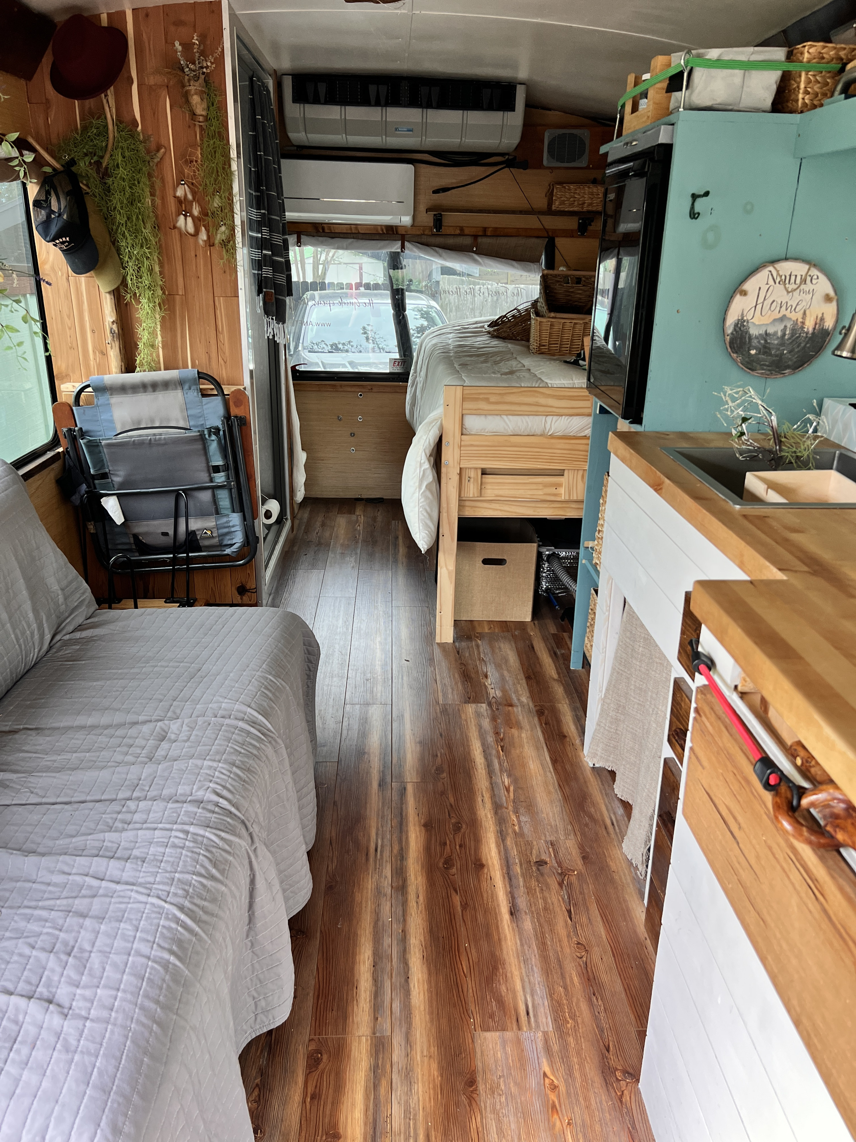 Inside a custom RV rental: wooden interior with a bed, daybed, kitchen, and two AC units visible.. Ford E-450 2016