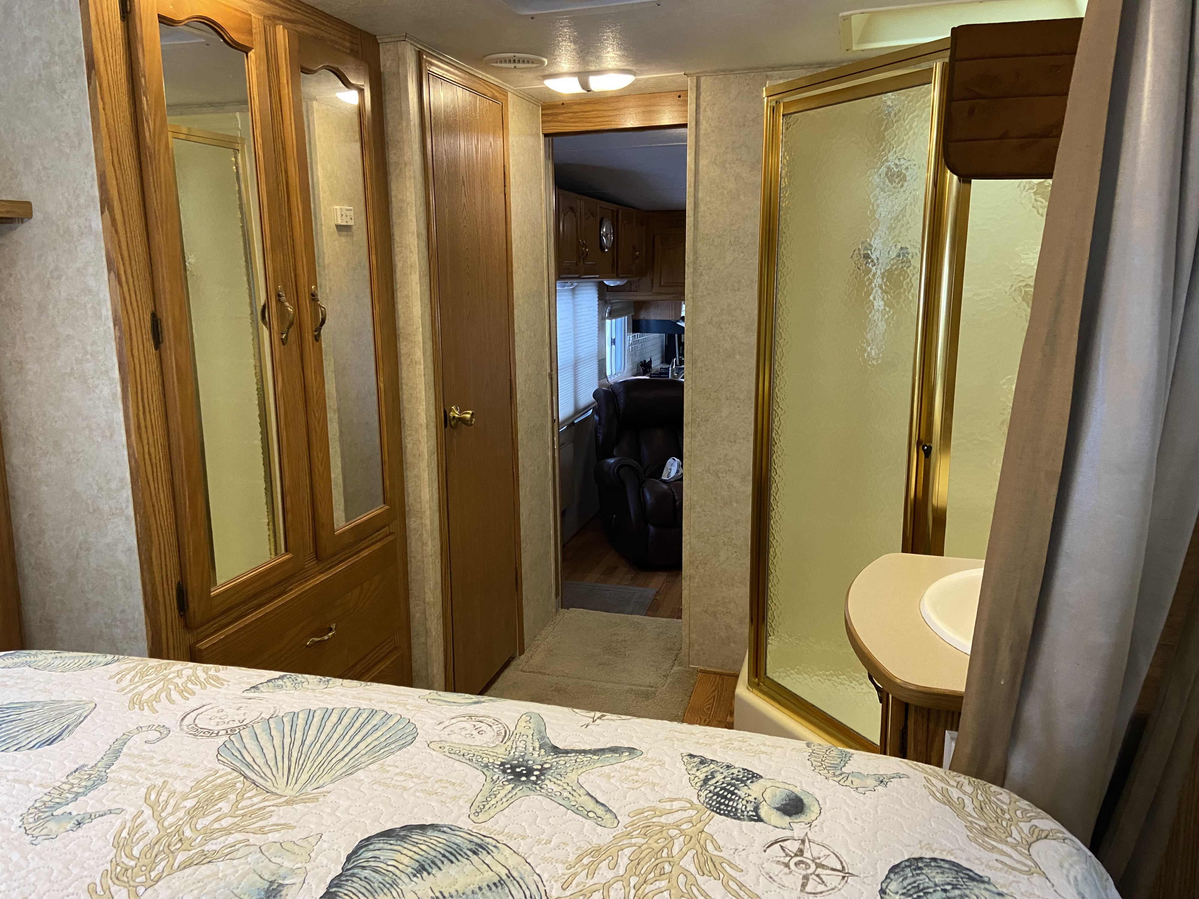 RV rental bedroom with seashell-patterned bedding, a mirrored wardrobe, compact shower, and a view into the living space.. Keystone RV Cougar 2005