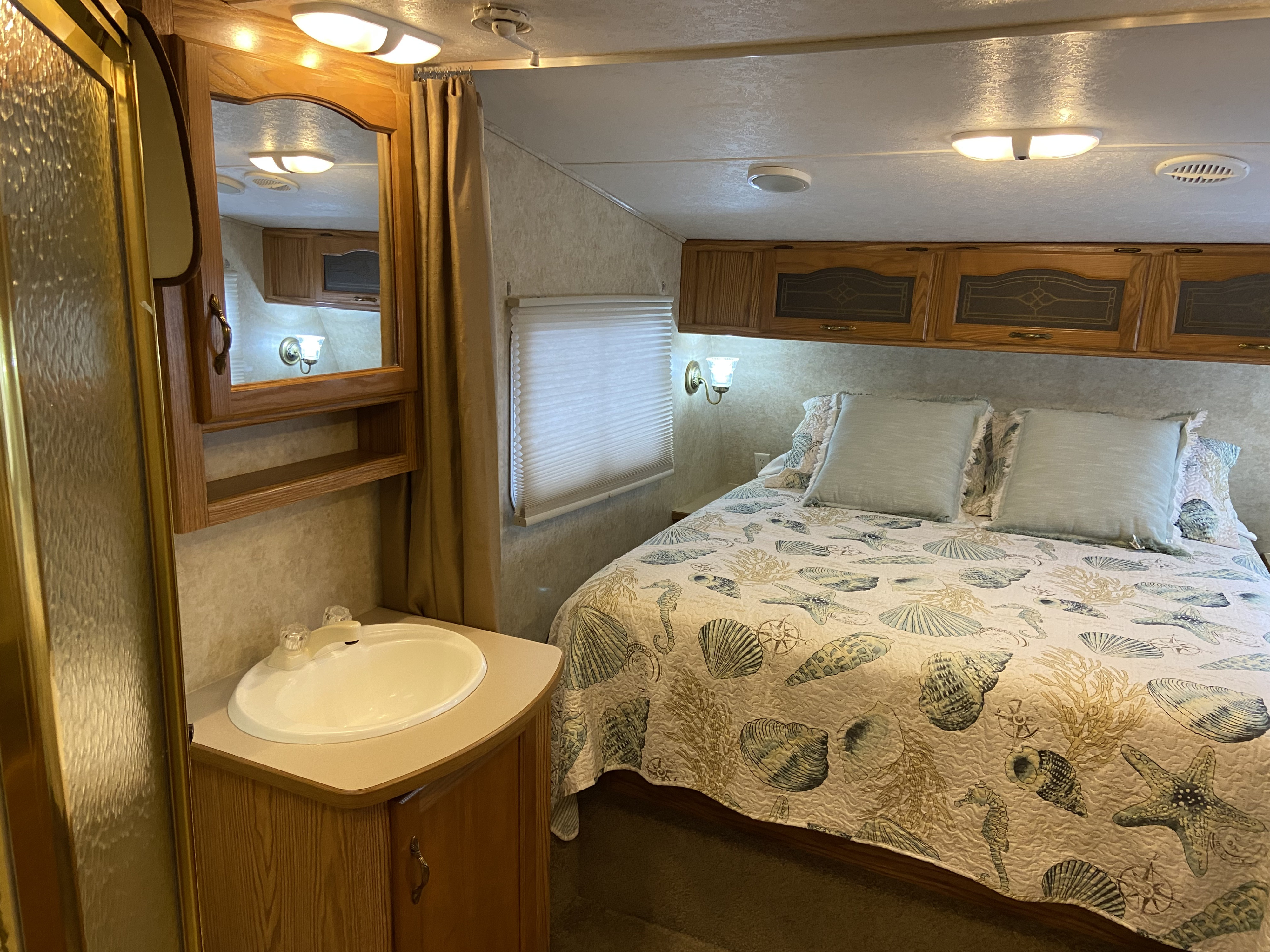 Cozy RV rental interior featuring a bedroom with nautical decor, overhead storage, and a private sink/vanity area. Ideal for your next trip.. Keystone RV Cougar 2005