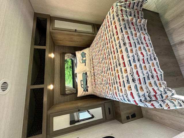 Bright RV rental bedroom featuring a bed with fun car-patterned comforter, storage shelves, and overhead cabinets.. Forest River Surveyor Legend 2022