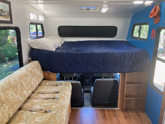 Cozy RV rental interior featuring a cab-over bed, patterned couch with seatbelts, and wooden storage shelves.. Dolphin 21 Foot 1989