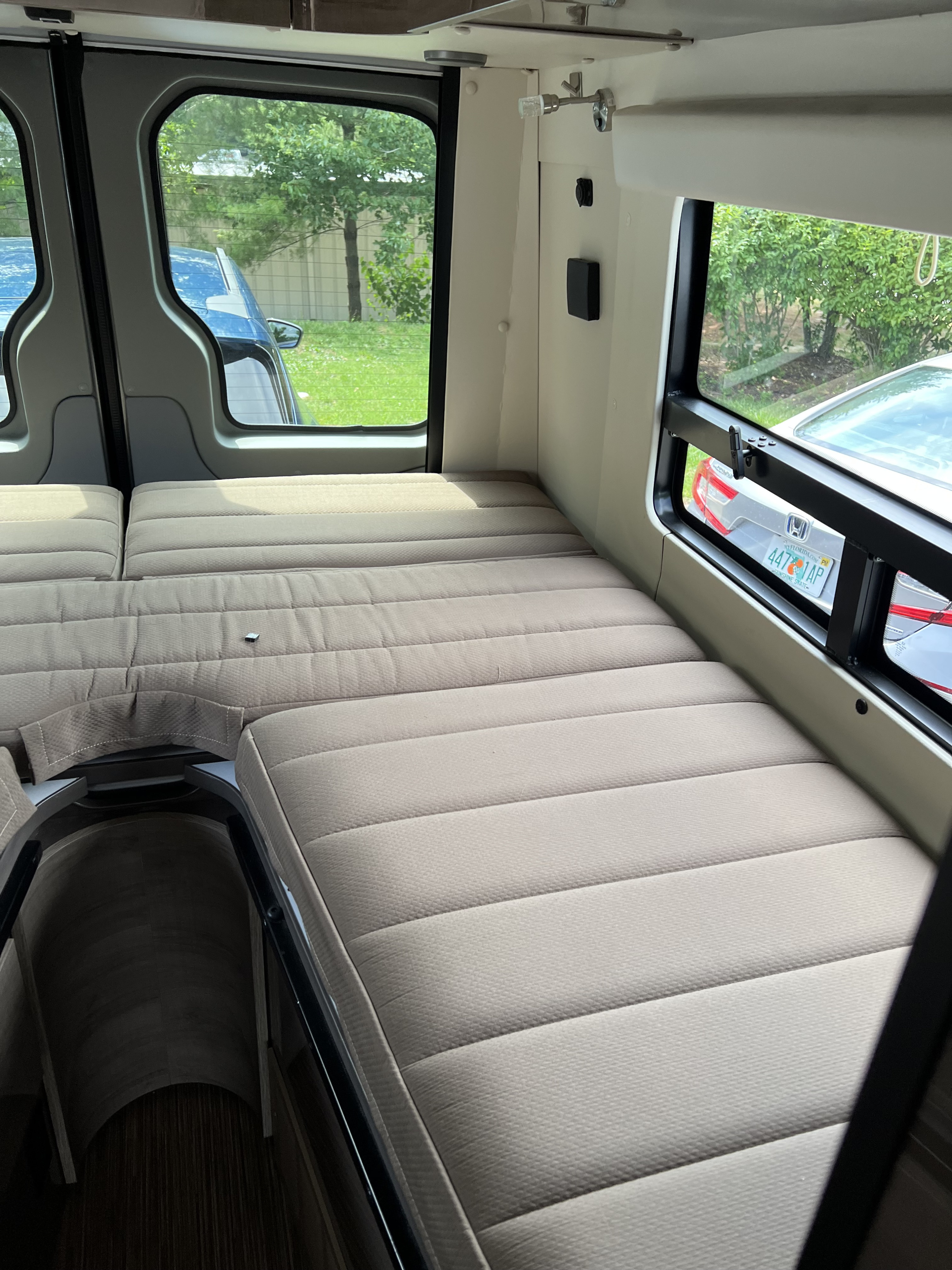 Interior of an RV rental: a plush, light-colored bed with modular cushions, flanked by large windows showing parked cars and trees.. ERA ERA Class B 2016