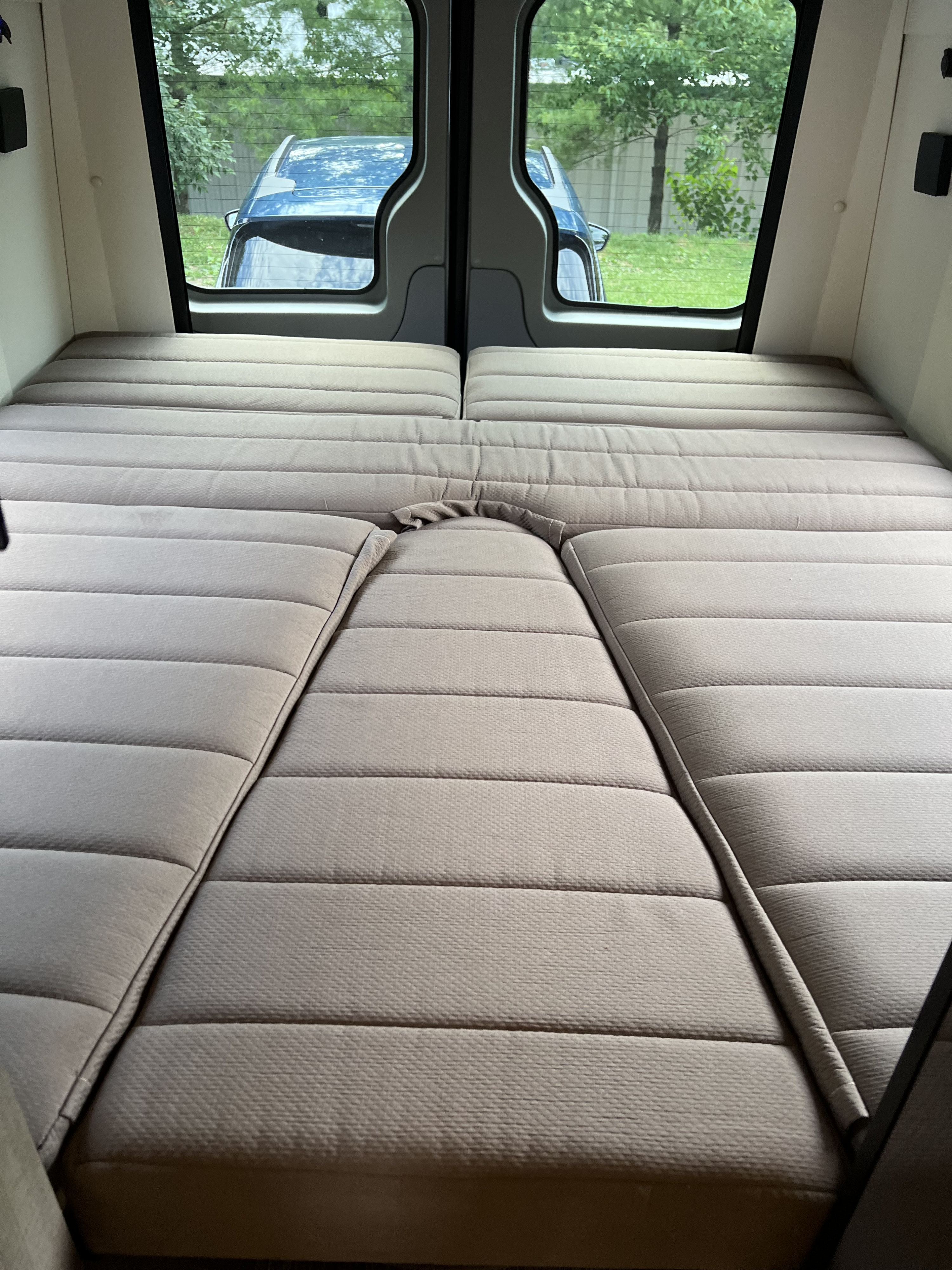 Comfortable modular bed in this rv rental, with a view of a car and trees through the rear windows.. ERA ERA Class B 2016
