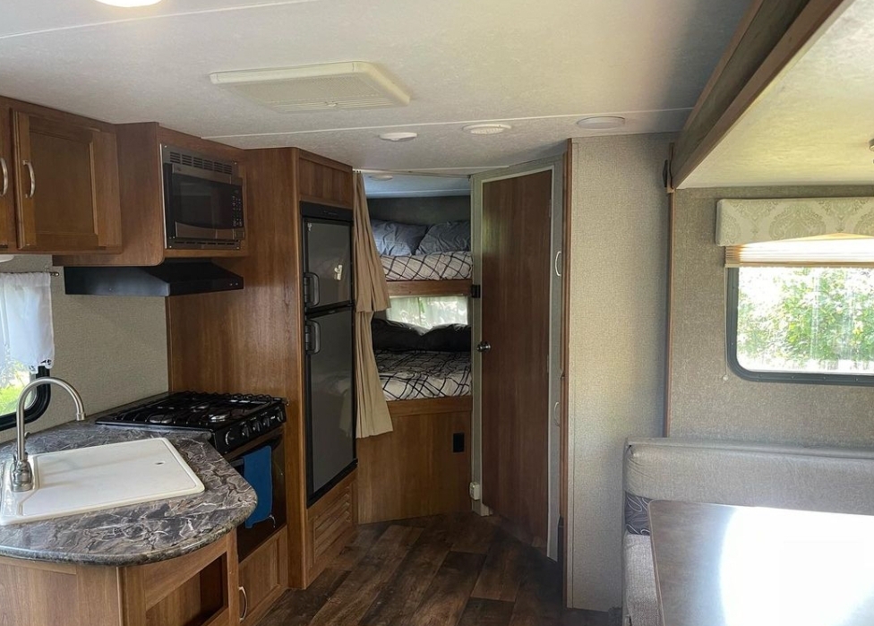 Inside an RV rental: kitchen with sink/stove, fridge, bunk beds, and dining nook. Compact and functional travel home.. Keystone RV Springdale 2018