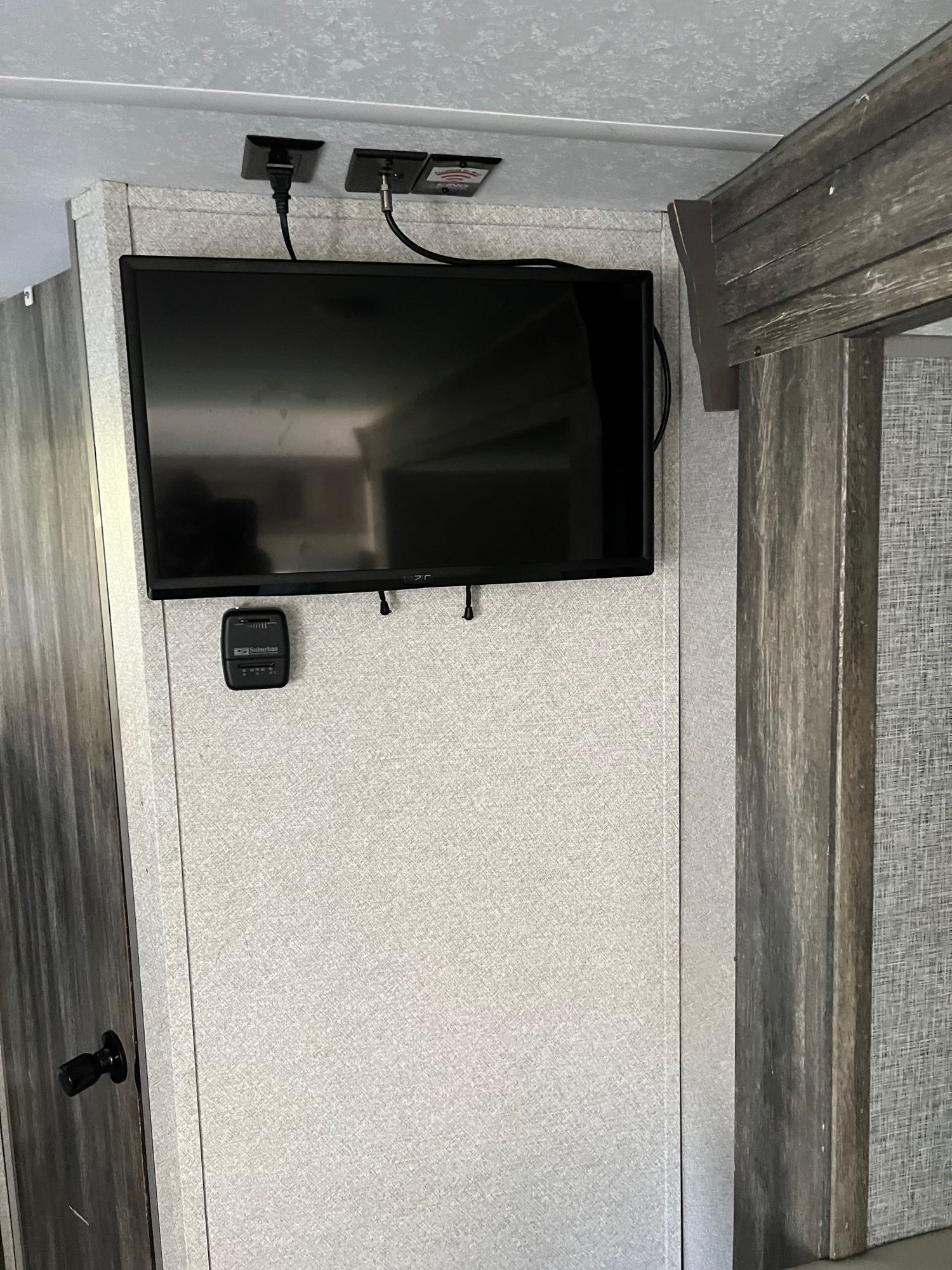 RV rental interior featuring a wall-mounted TV, power outlets, and a Suburban thermostat on textured gray walls.. Forest River Wildwood FSX 2020