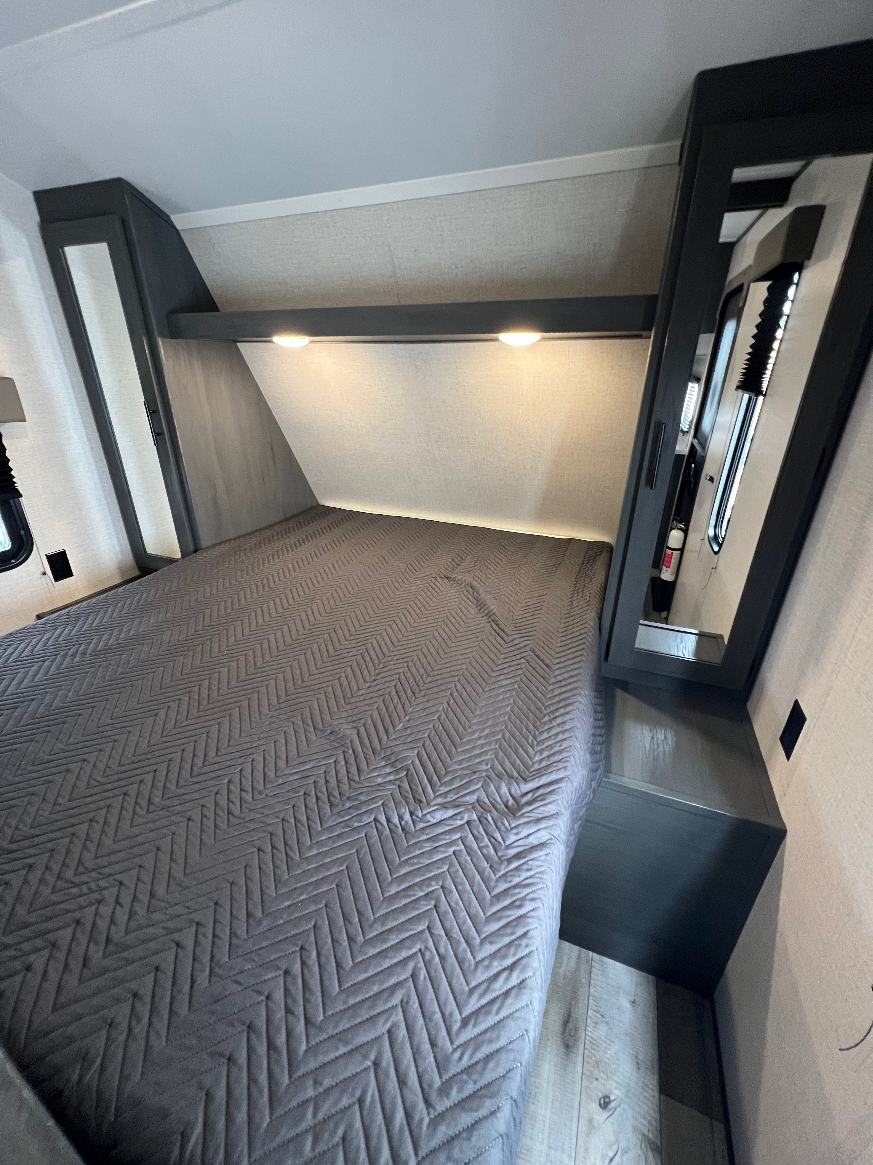 Modern RV rental bedroom showcasing a gray quilted bed, overhead lights, and built-in storage.. Dutchmen Aspen Trail 2022