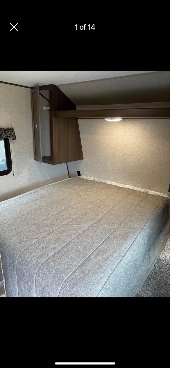 Cozy RV rental bedroom features a comfortable bed with grey bedding, overhead storage, and soft lighting for your travels.. Keystone RV Springdale 2019