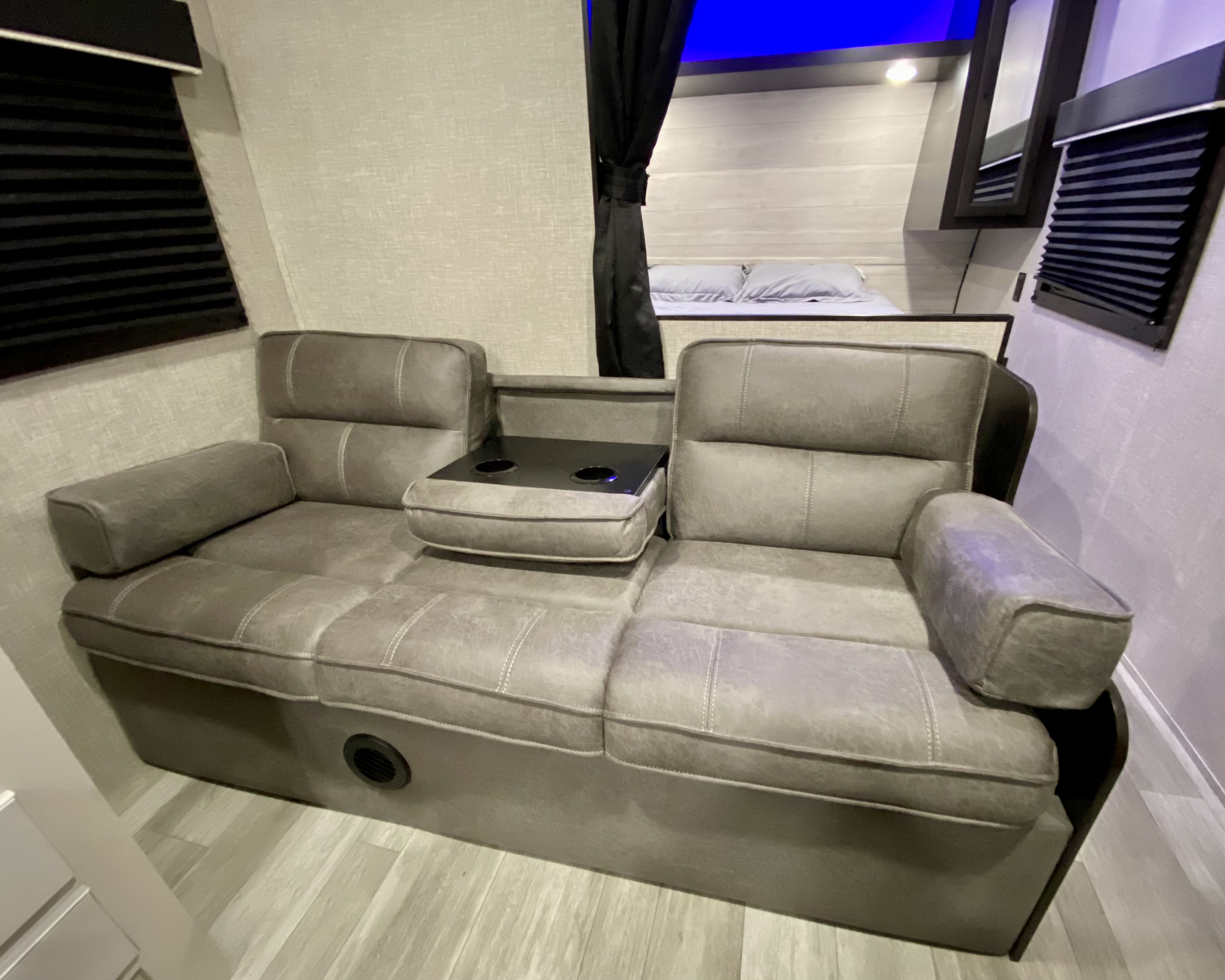Cozy gray RV rental living space featuring a reclining sofa with a center console and cup holders, next to a comfortable bed.. Jayco Jay Flight 2023