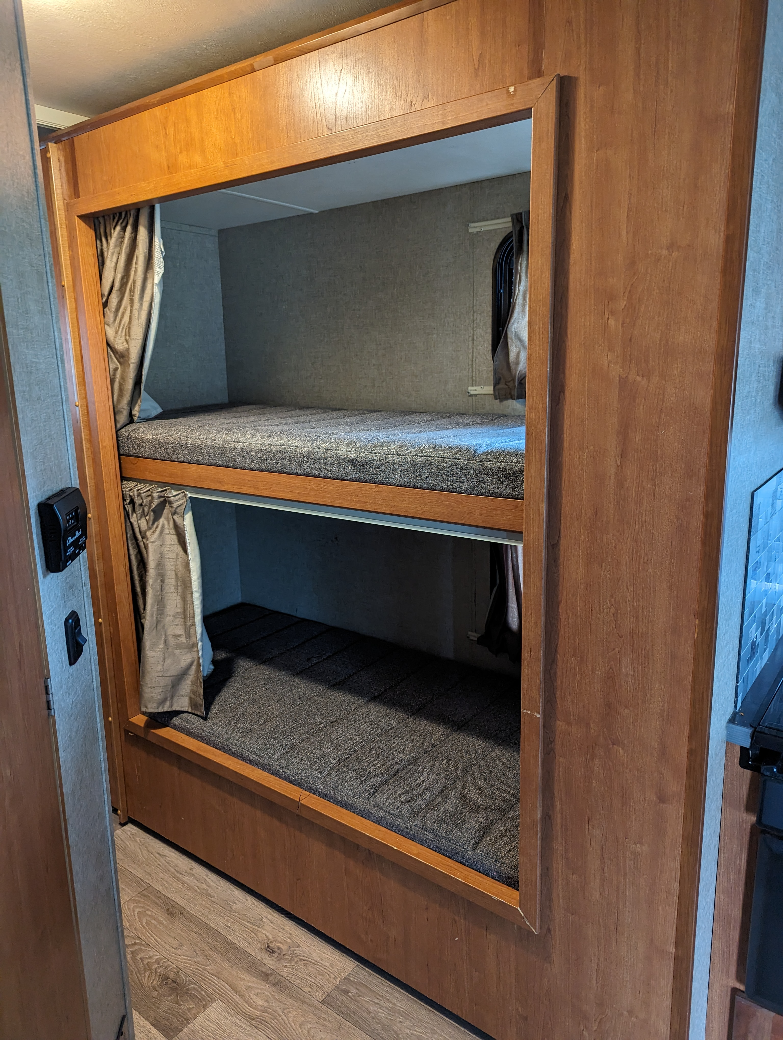 Stacked bunk beds with grey mattresses and privacy curtains inside an RV rental, featuring warm wood trim.. Winnebago Spirit 2019