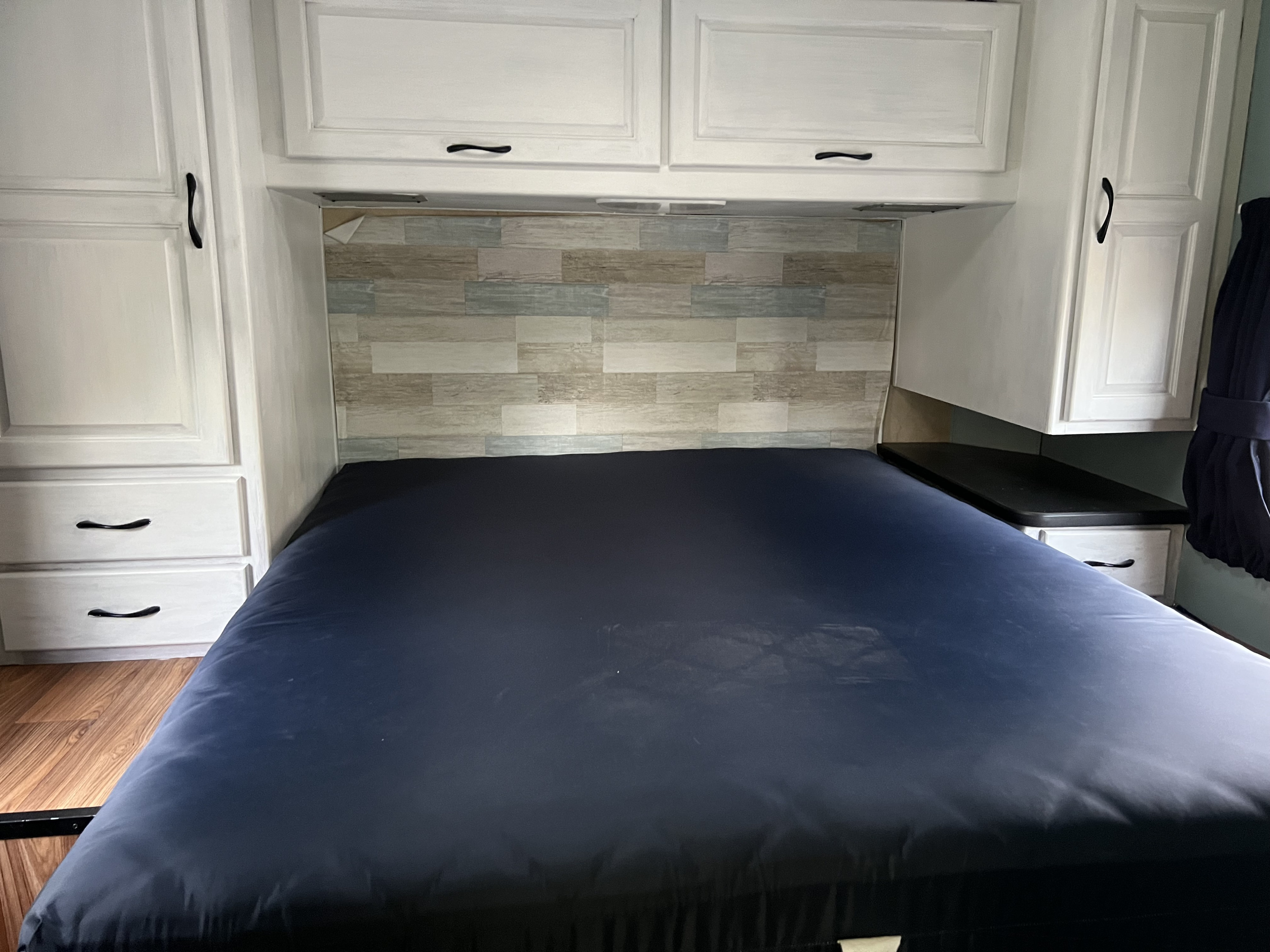 Comfortable RV rental bedroom with dark blue bed, white cabinets, and a multi-toned wood headboard.. Thor Majestic 2013