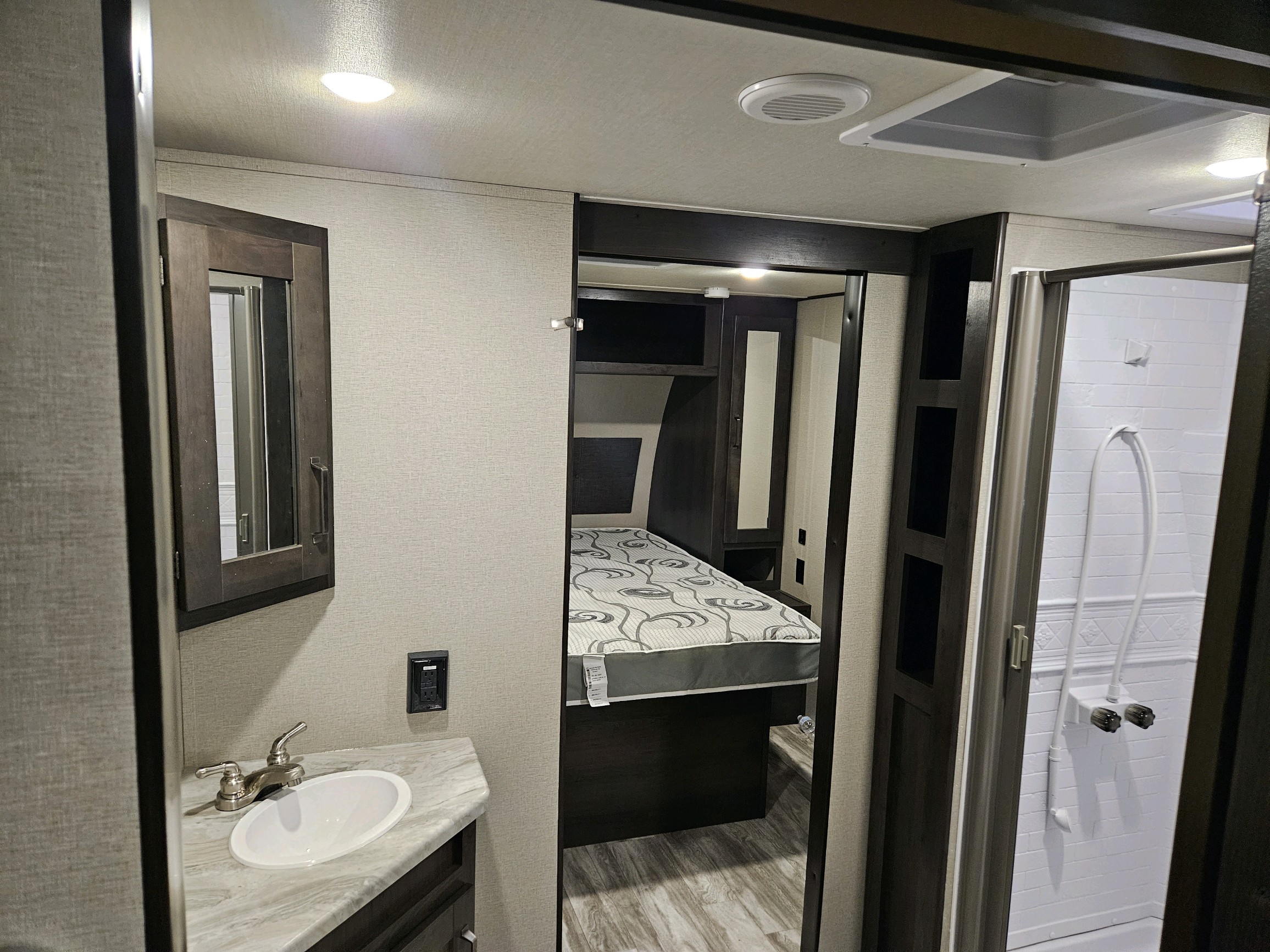 RV rental interior showcasing a compact bathroom with sink and mirror, a bedroom with bed, and a separate shower stall.. Grand Design Transcend Xplor 2022