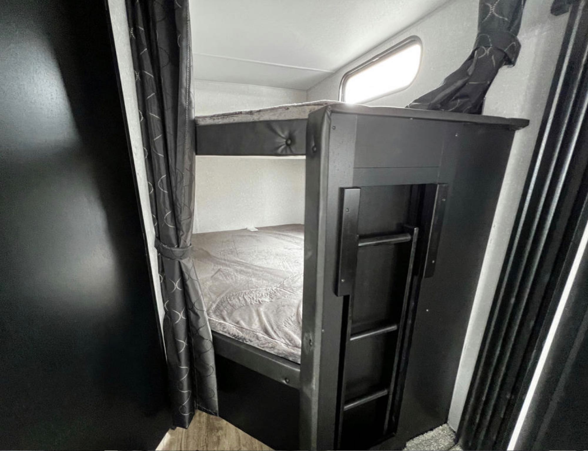 Inside an RV rental: bunk beds with light bedding, window, & ladder. Cozy and practical sleeping space for travel.. Forest River Cherokee 2022