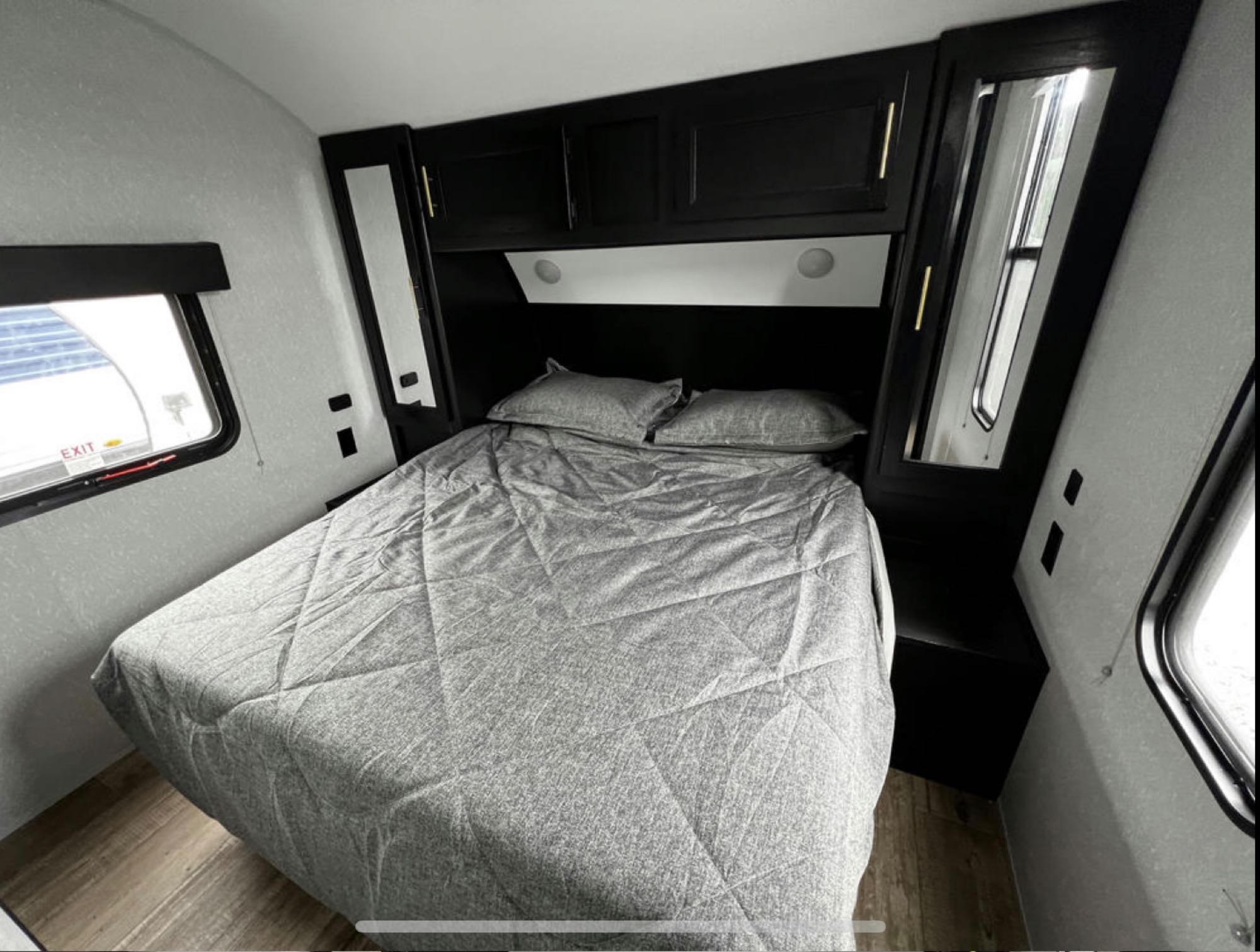RV rental: a compact bedroom with gray bed, dark overhead cabinets, reading lights, and side windows.. Forest River Cherokee 2022
